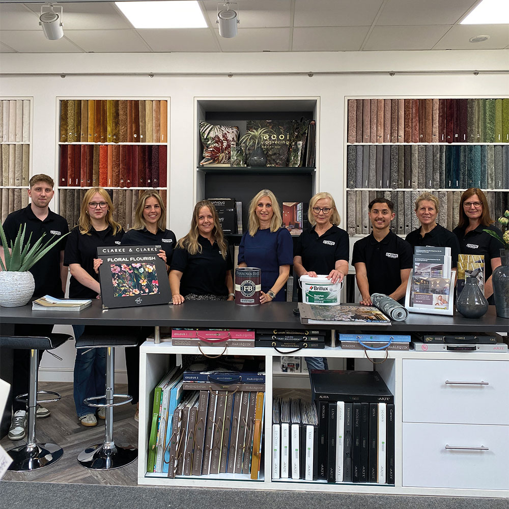 Team im Fachmarkt Reken am Beratungstresen, dahinter Tapetenmuster und Regale mit Mustermappen