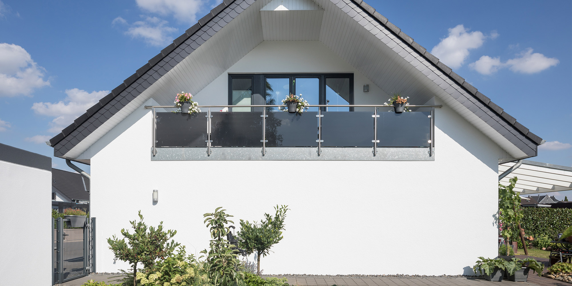 Weiß verputzte Hausfassade mit Balkon und dunklem Geländer vor blauem Himmel