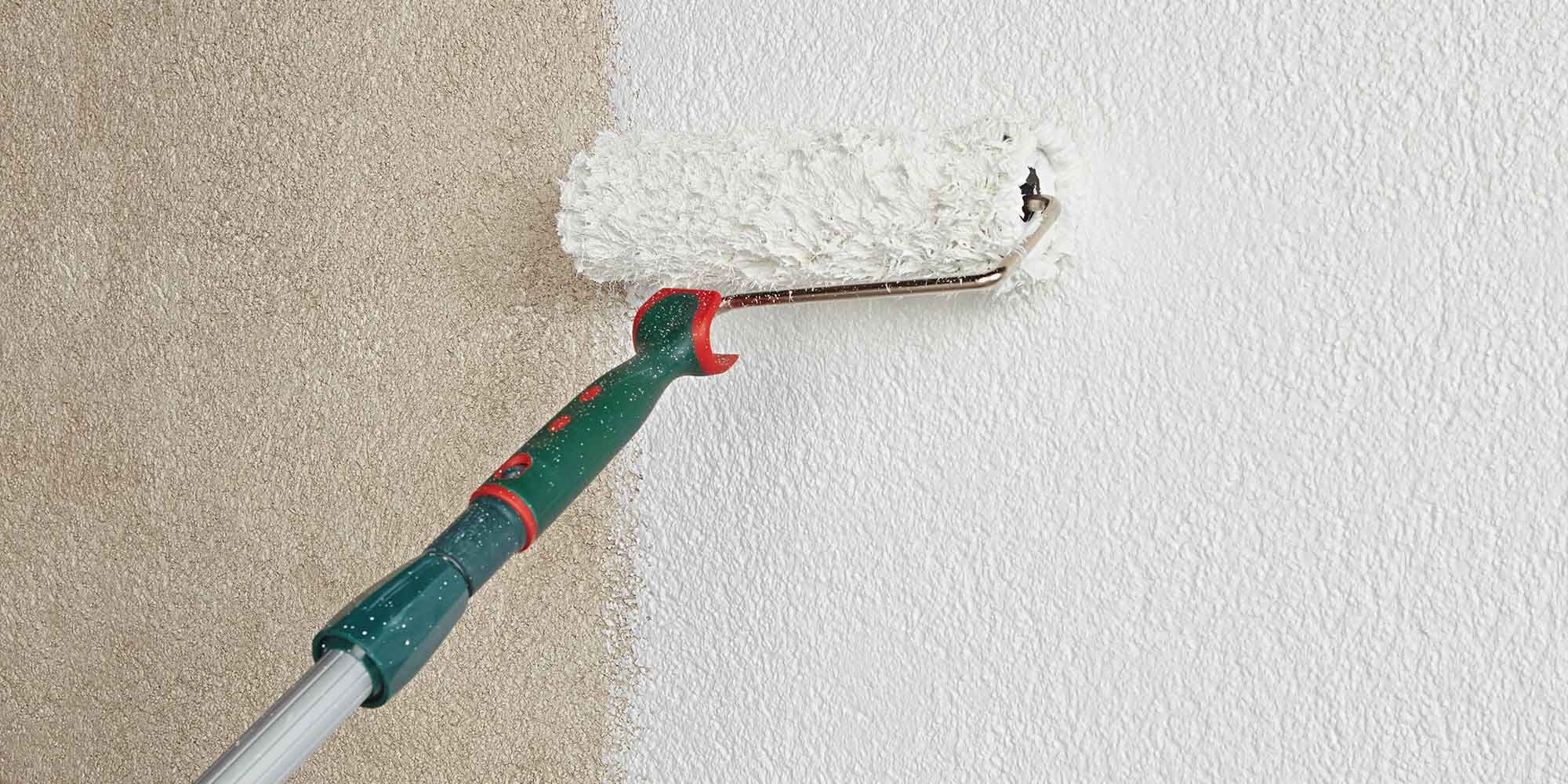 Farbrolle streicht eine strukturierte Wand gleichmaessig weiss als Untergrund Vorbereitung