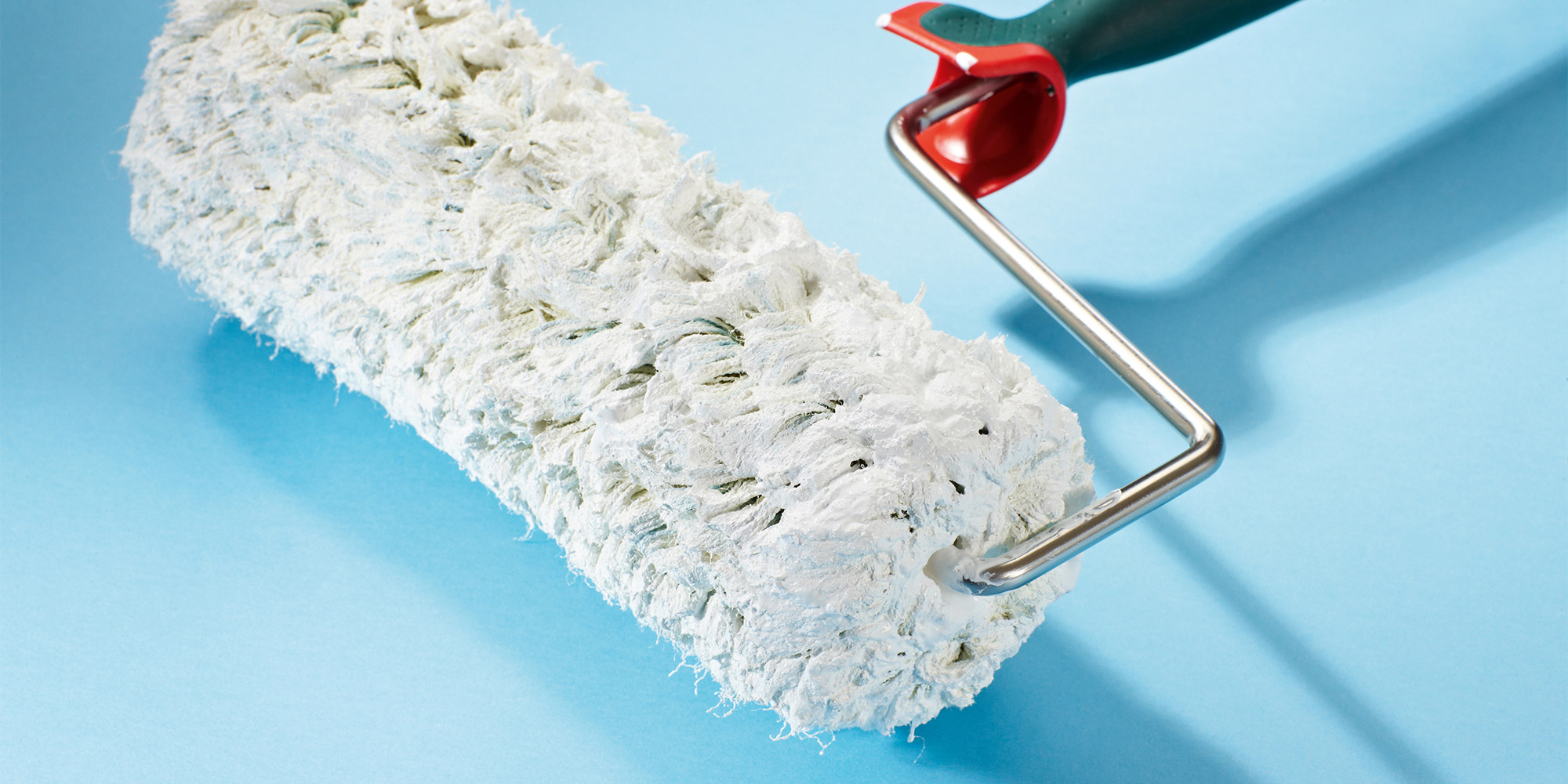 Farbrolle auf blauem Hintergrund, Detailaufnahme eines Werkzeugs zum Streichen grosser Flaechen