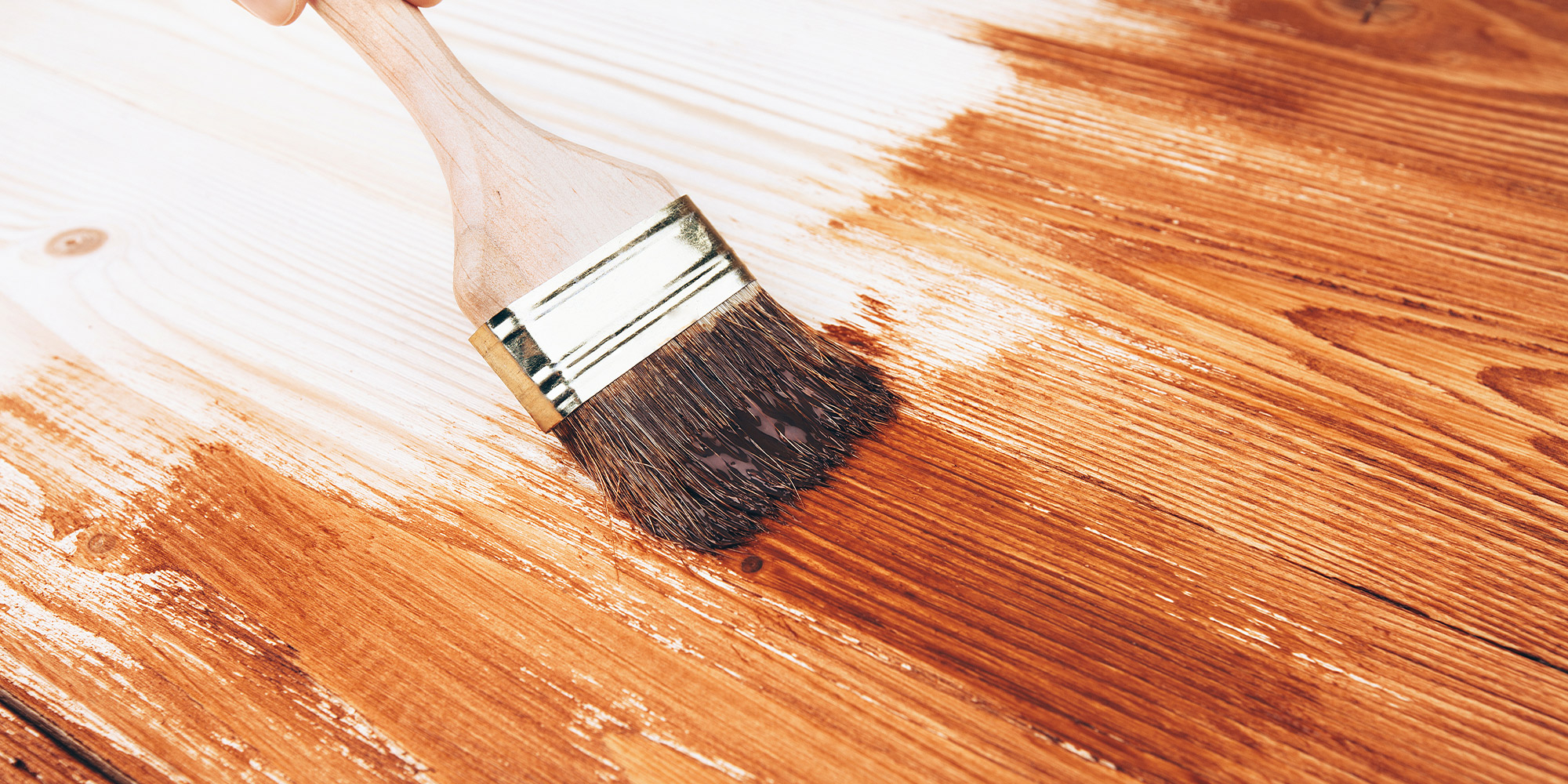 Flacher Pinsel trägt Sikkens Holzlasur auf eine Holzoberfläche auf