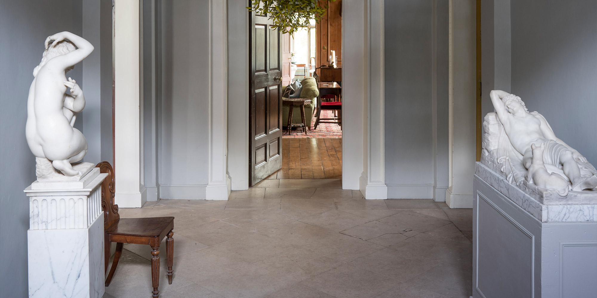 Flur mit grauen Wänden, Skulpturen auf Sockeln und Blick in einen angrenzenden Raum