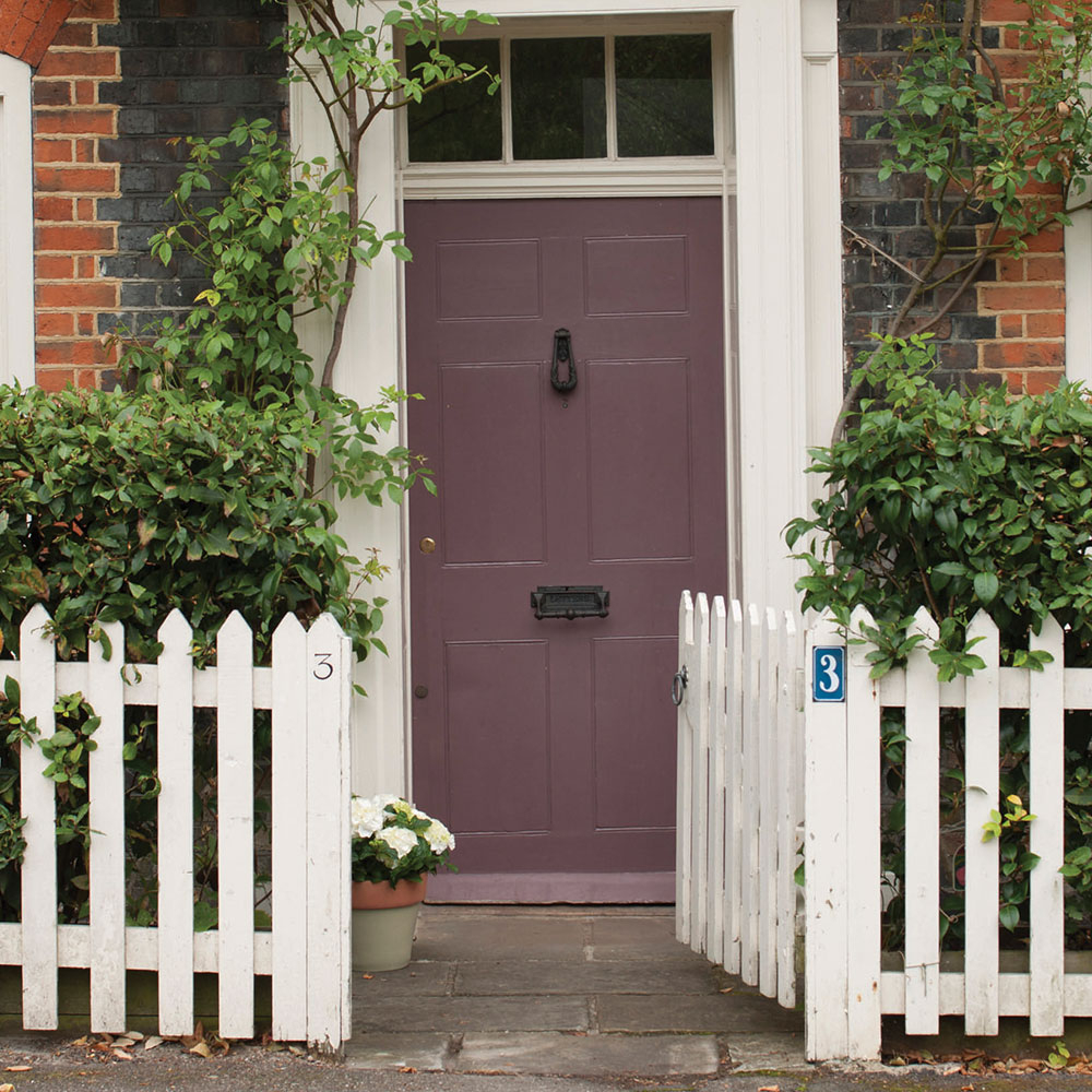 Violettgraue Haustür hinter weißem Gartenzaun mit viel Grün - ruhige Farbidee für den Türanstrich
