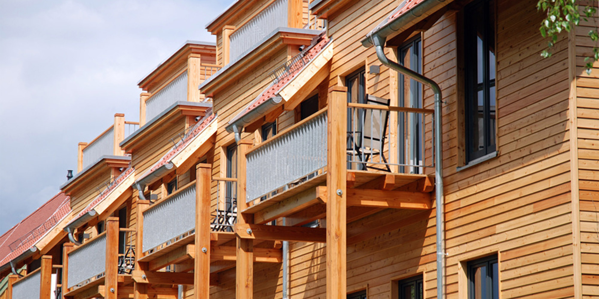 Fassade eines modernen Mehrfamilienhauses mit Holzverkleidung und Balkonen, sonniger Tag