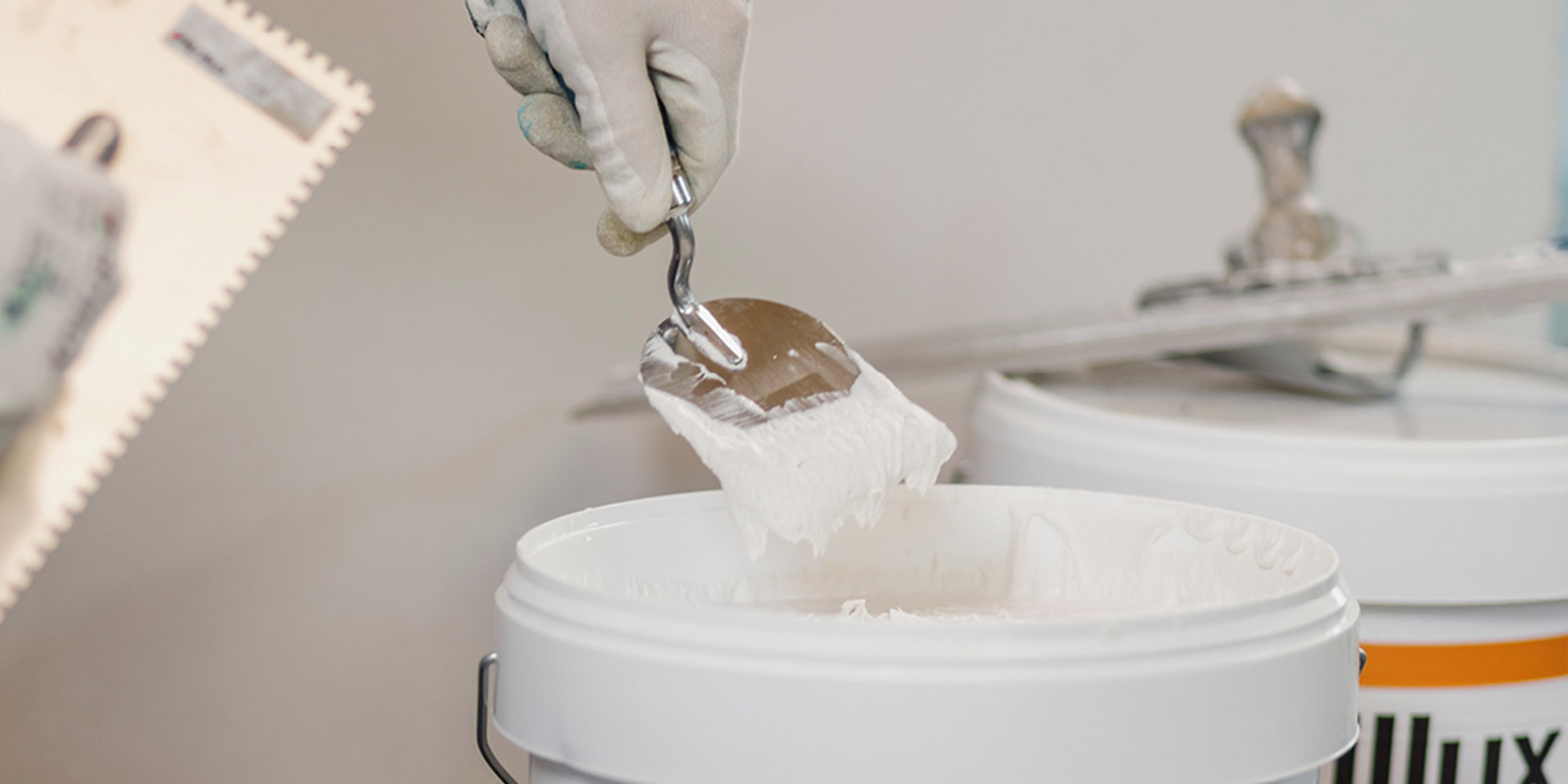 Kelle entnimmt Spachtelmasse aus einem Eimer, Werkzeug für saubere Spachtelarbeiten