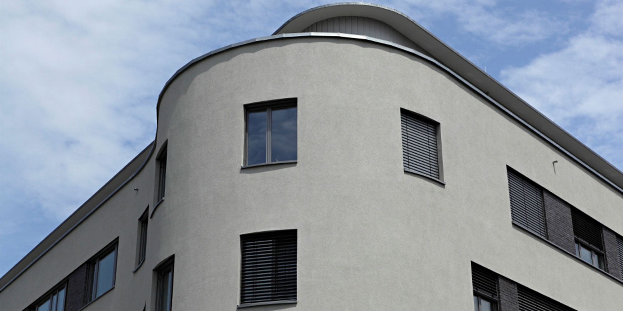 Gebäude mit abgerundeter Ecke und grauer Putzfassade, moderne Fenster mit Sonnenschutz