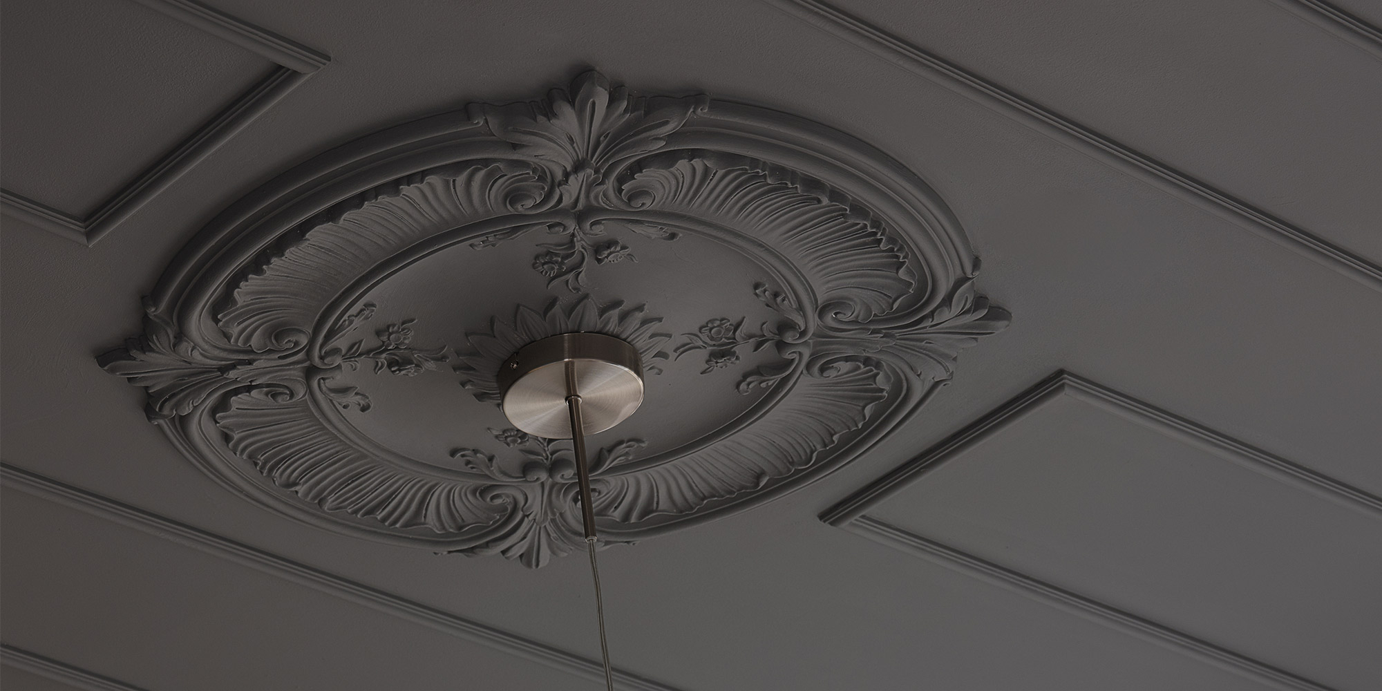 Dekorative schwarze Stuckrosetten unter einer schwarzen Zimmerdecke heben Pendelleuchten hervor.