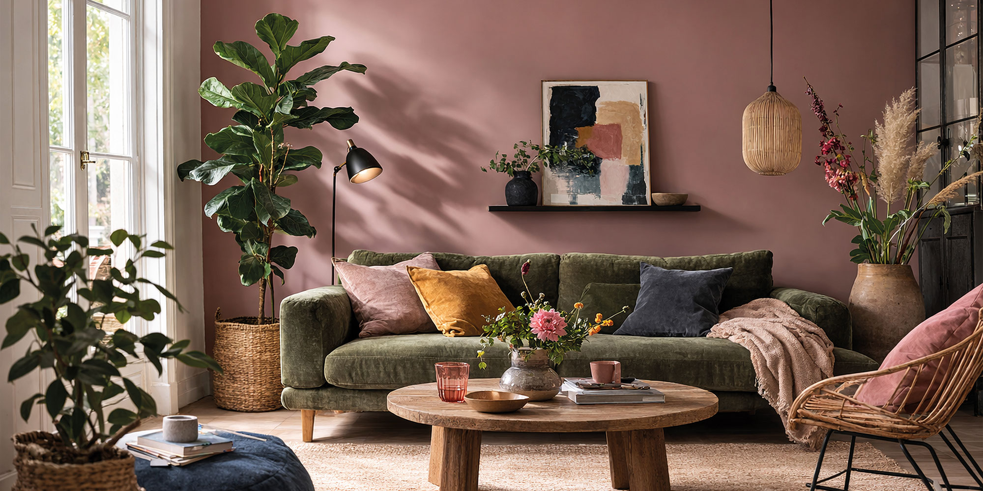 Wohnzimmer mit rosa Wand, grünem Sofa, Wandregalen und Pflanzen am Fenster