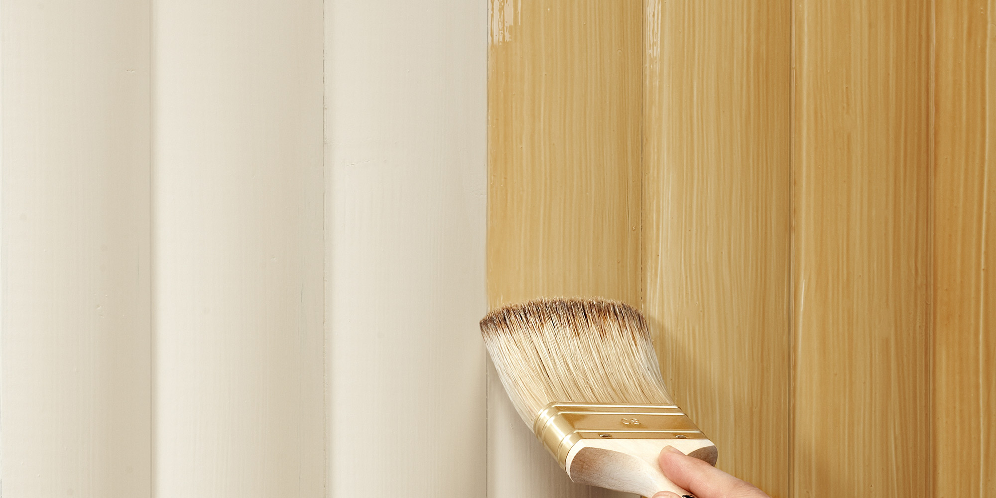 Hand lackiert eine Holzfläche mit einem breiten Pinsel, der frische Lack verleiht dem Holz einen warmen Glanz