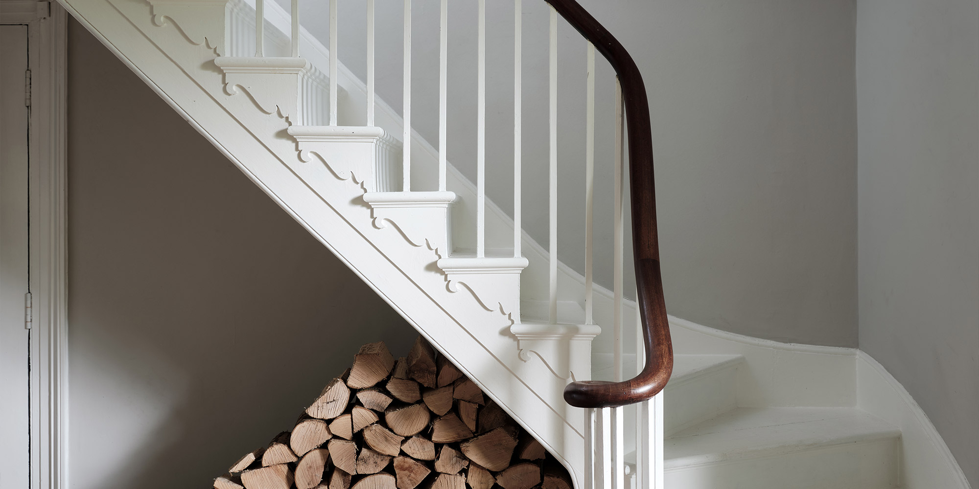 Weißes Treppengeländer mit Holzhandlauf und gestapeltem Brennholz unter der Treppe