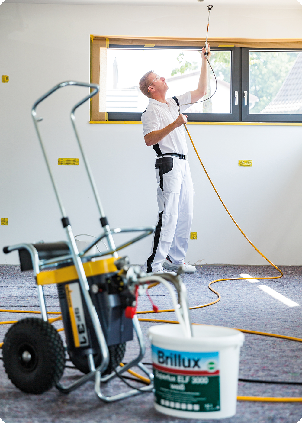 Ein Maler der eine Zimmerdecke mit Brillux Superlux ELF 3000 spritzt, davor ein Farbeimer.