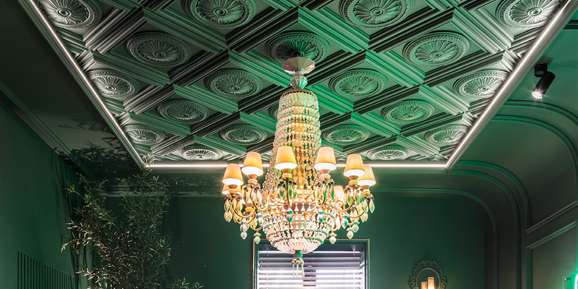 Dekorativ gestaltetes Esszimmer mit floralen und klassischen dunkelgrünen Stuckrosetten unter der Decke.