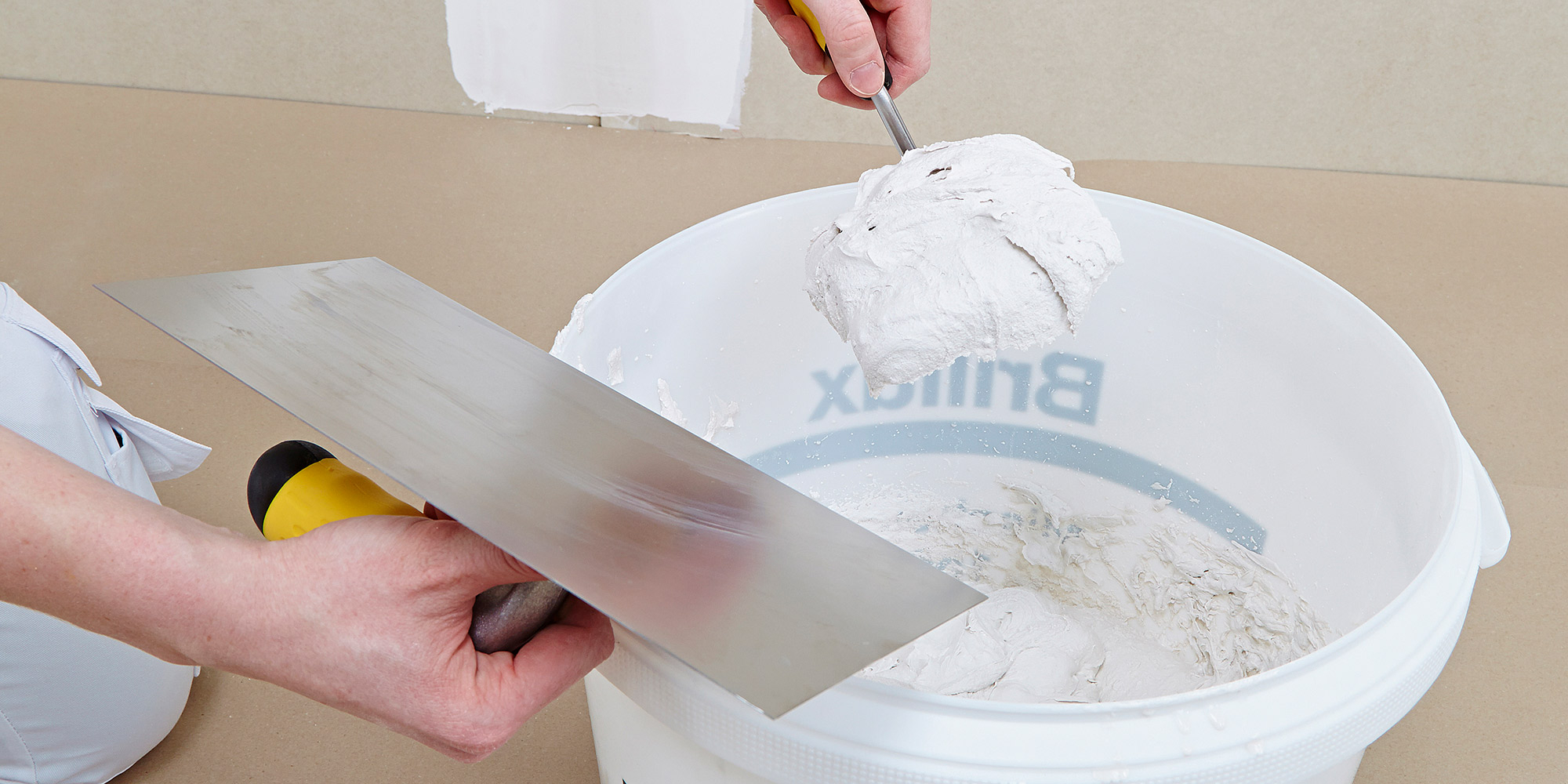 Spachtelmasse wird aus dem Eimer entnommen und auf eine Glättkelle aufgenommen