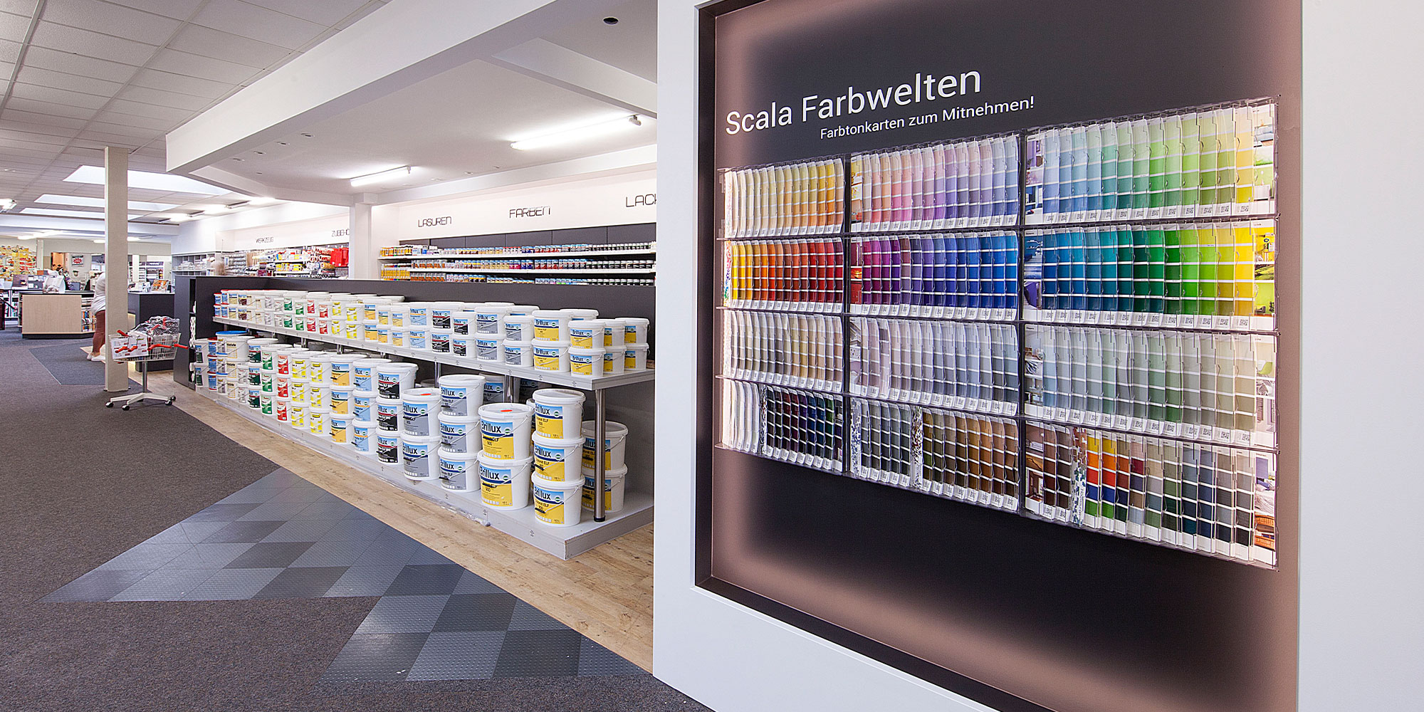 Farbtonwand im Fachmarkt mit vielen Farbtonkarten und Regal mit Farbeimern zur Wunschfarbtonwahl