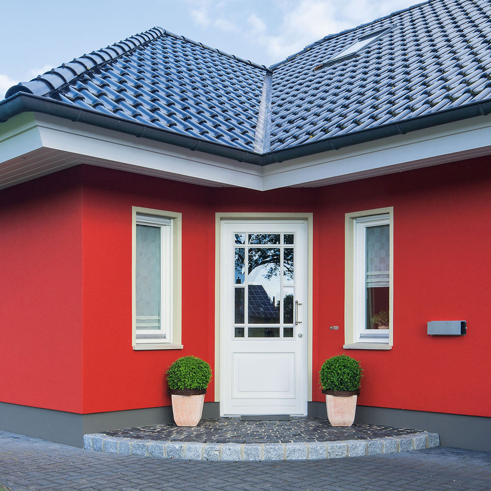 Haus mit roter Fassade und weißer Haustür, flankiert von Fenstern und zwei Kugelsträuchern - Beispiel Außenanstrich