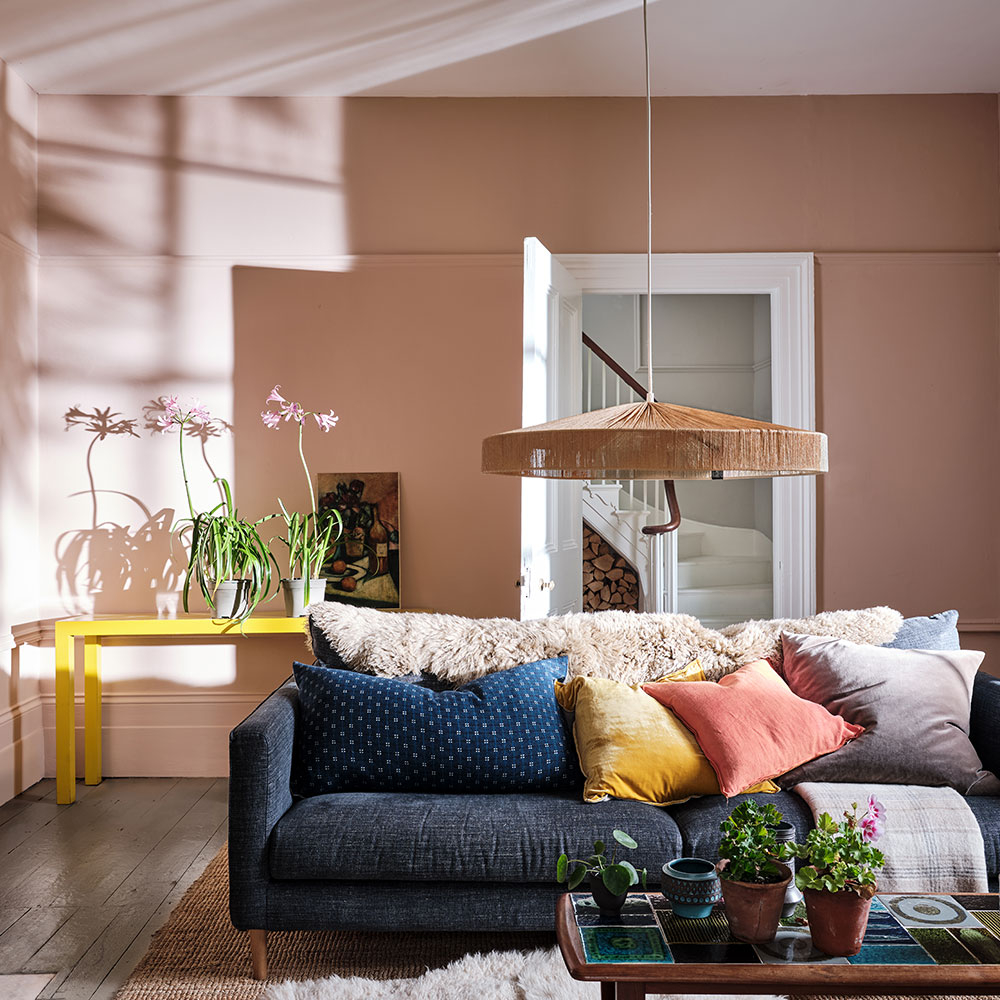 Wohnzimmer mit rosabeiger Wand, Sofa und Kissen im Sonnenlicht - Inspiration für Wunschfarbton