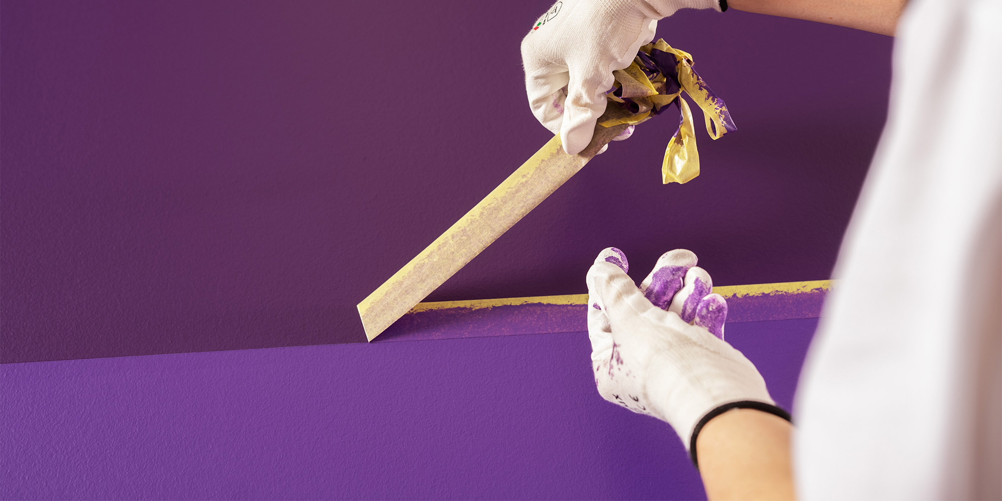 Hand entfernt Malerkrepp an violetter Wand, Vorbereitung für einen Anstrich mit Silikat Innenfarbe