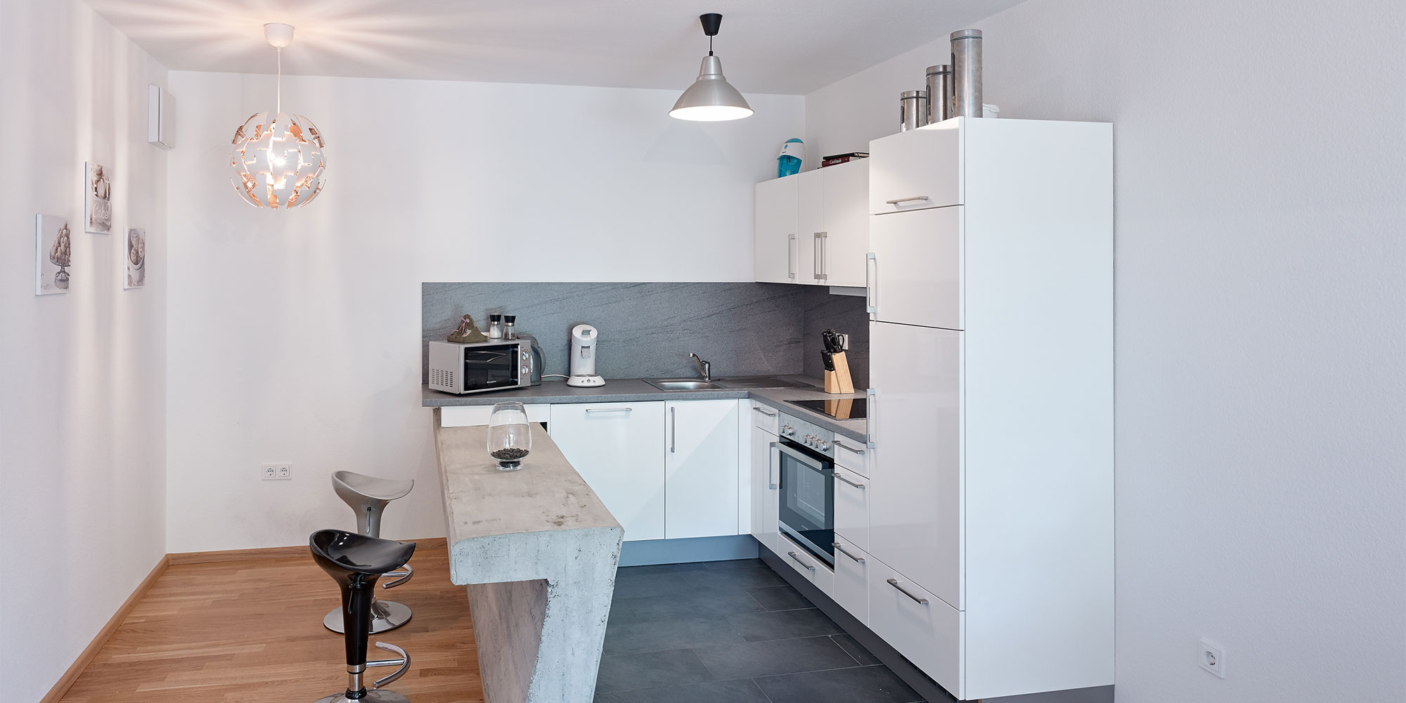 Moderne Küche mit weißen Fronten, grauer Arbeitsplatte und Kücheninsel aus Beton