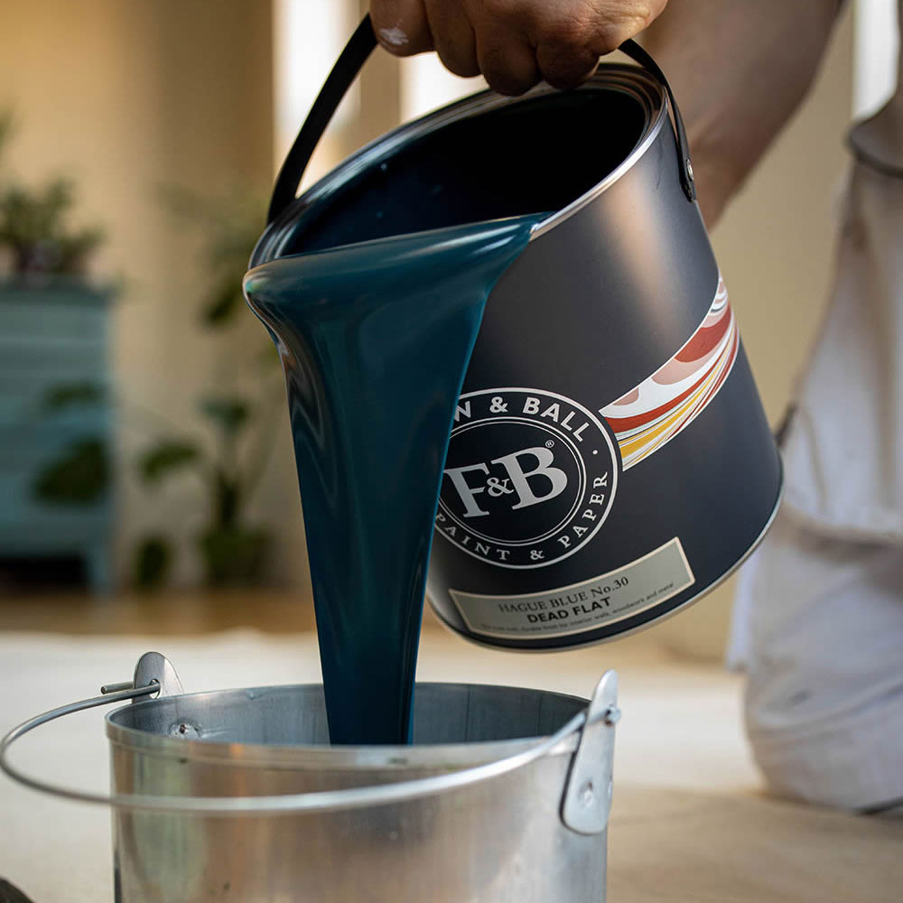 Dunkelblauer Lack wird aus einer Dose in einen Metalleimer gegossen, Vorbereitung zum Möbel streichen