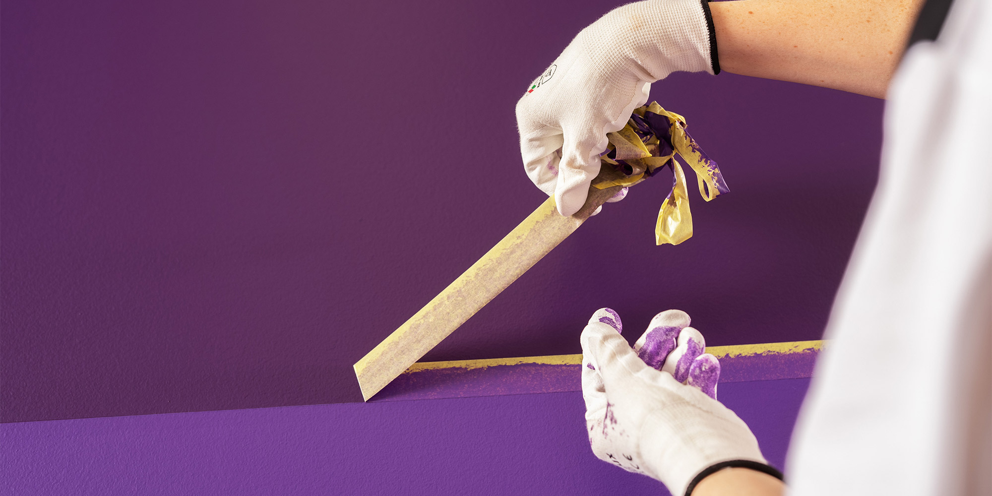 Handschuhe ziehen Malerkrepp von violett gestrichener Wand ab für eine saubere Farbkante