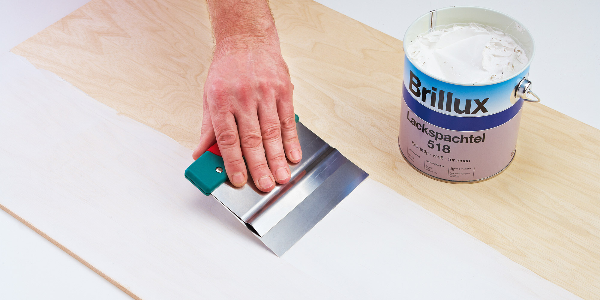 Spachtel verteilt Brillux Lackspachtel 518 auf Holzplatte, glatte weiße Schicht entsteht