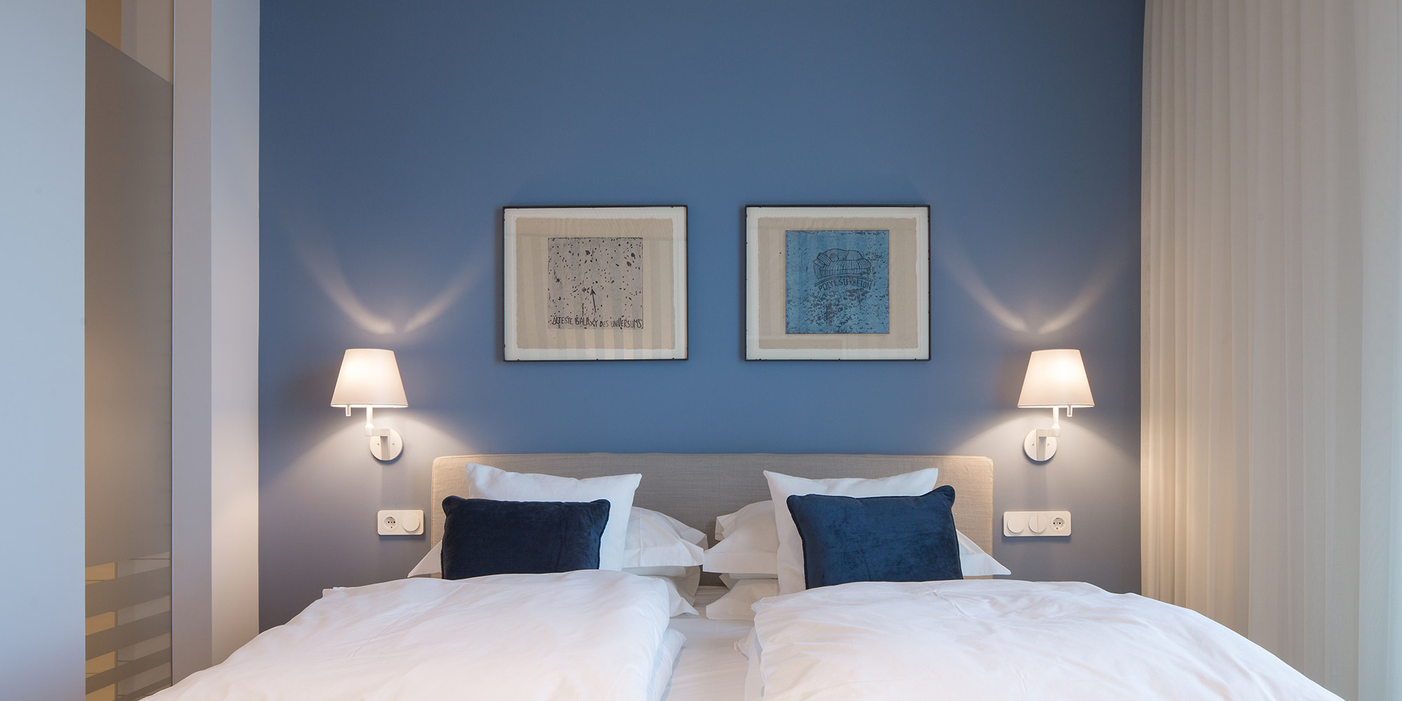 Schlafzimmer mit blau gestrichener Wand und zwei Betten, ruhige glatte Wandfläche