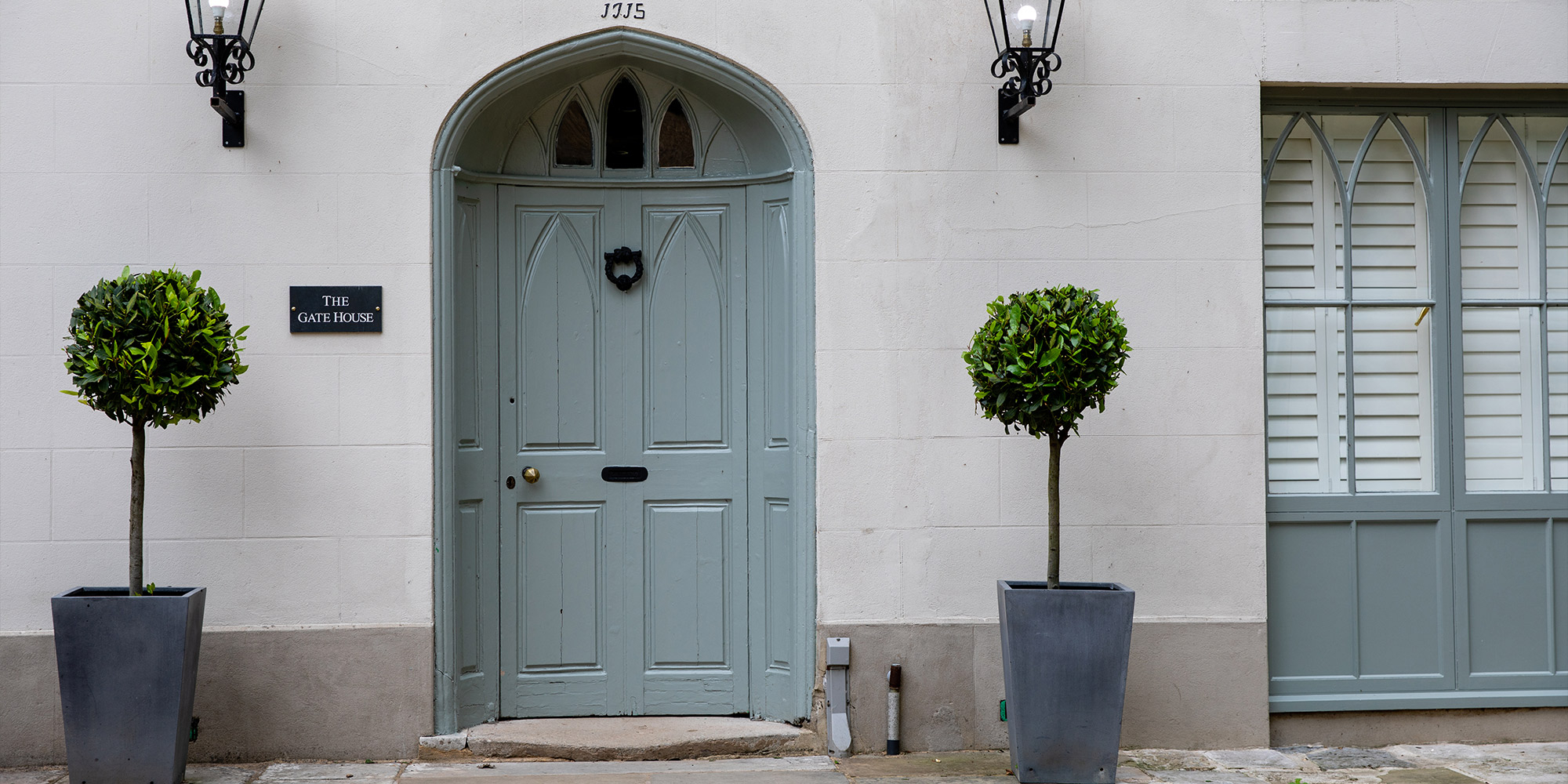 Hellblaue Haustür in Rundbogenform mit zwei Pflanzkübeln vor heller Fassade
