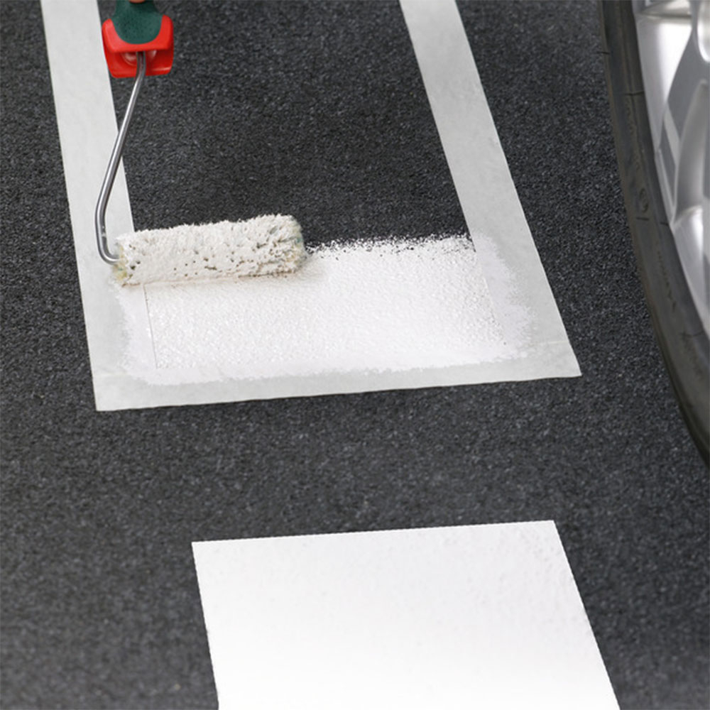 Farbroller trägt weiße Beschichtung in abgeklebter Fläche auf dunklem Boden auf - Markierungsfarbe für Böden