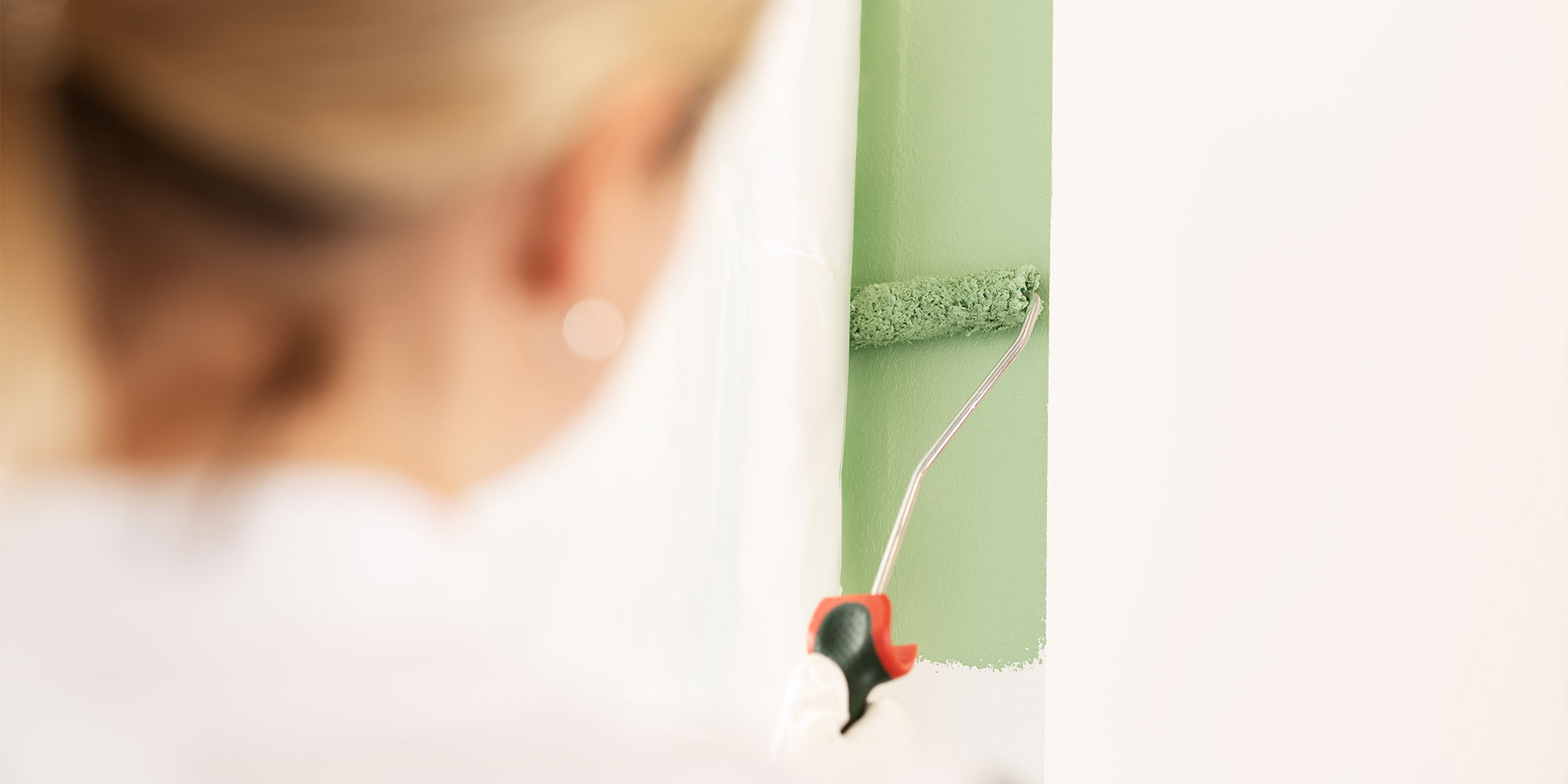 Farbrolle traegt gruene Wandfarbe auf eine abgegrenzte Flaeche auf - Beispiel fuer FAQ zu sauberem Anstrich