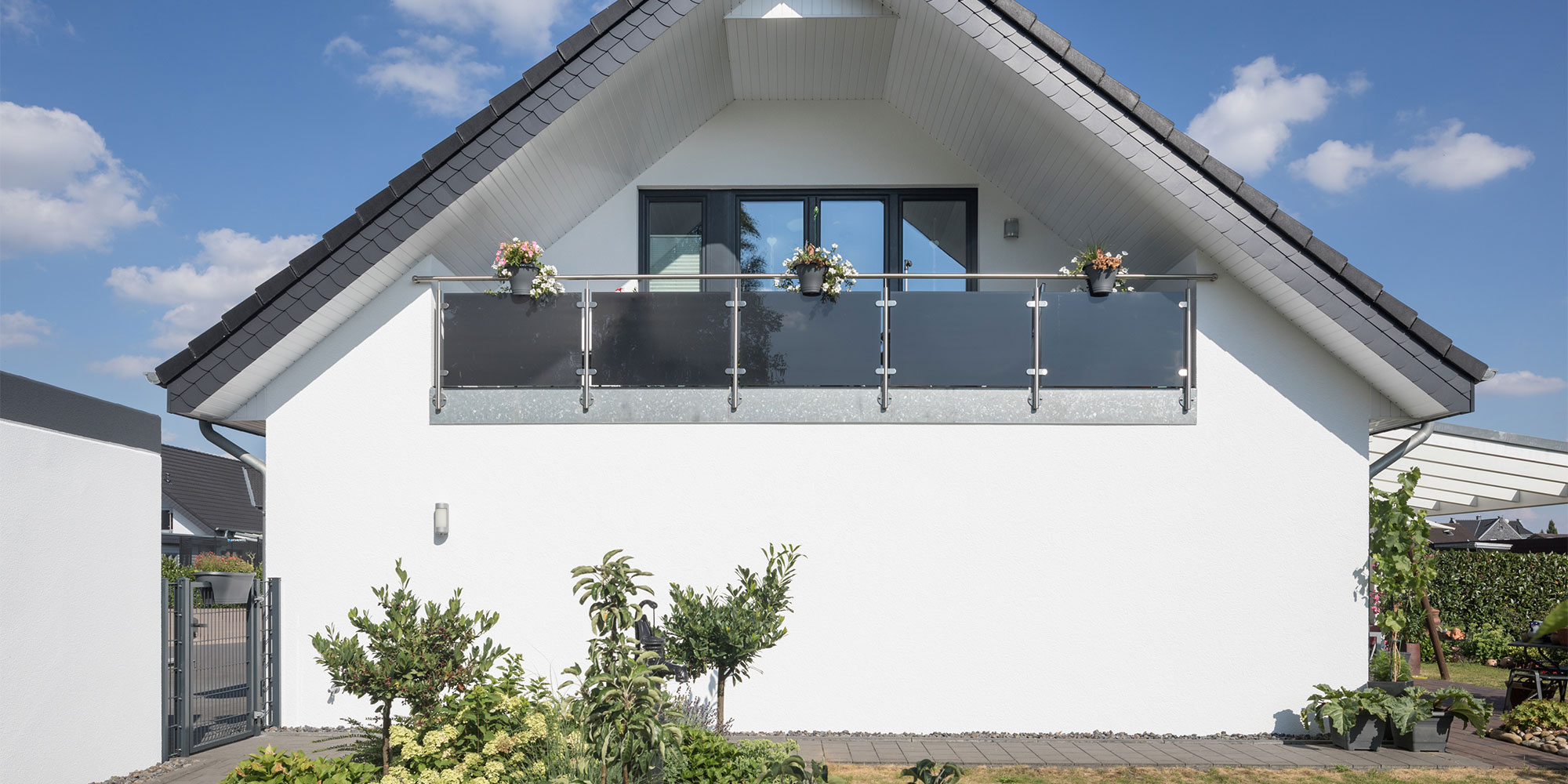 Hausfassade mit Balkon und weißem Putz vor blauem Himmel