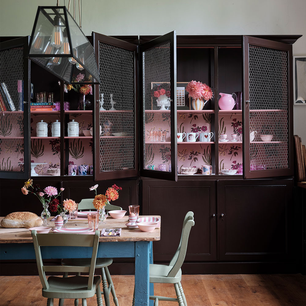 Dunkelbrauner Wohnzimmerschrank mit Gittertüren, rosa Innenflächen und dekoriertem Esstisch davor