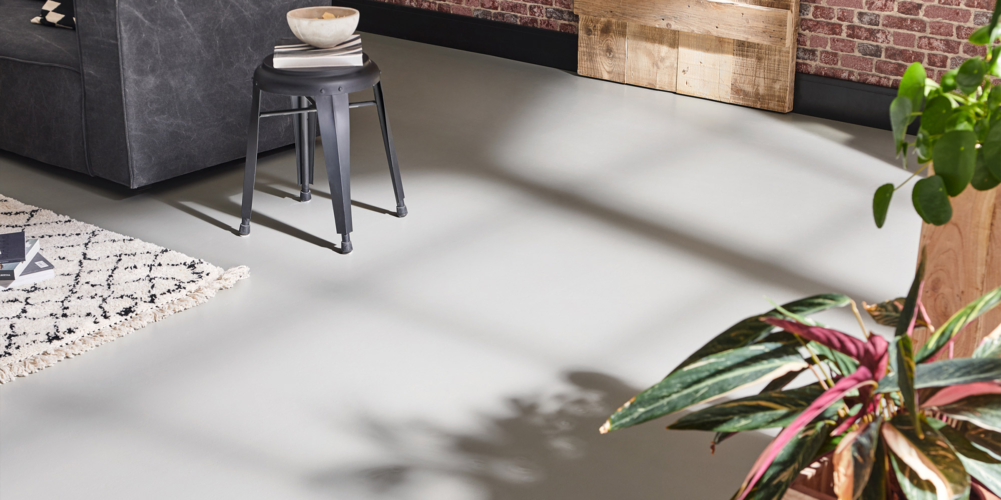 Heller Boden im Wohnbereich mit Hocker, Teppich, Pflanzen und Backsteinwand