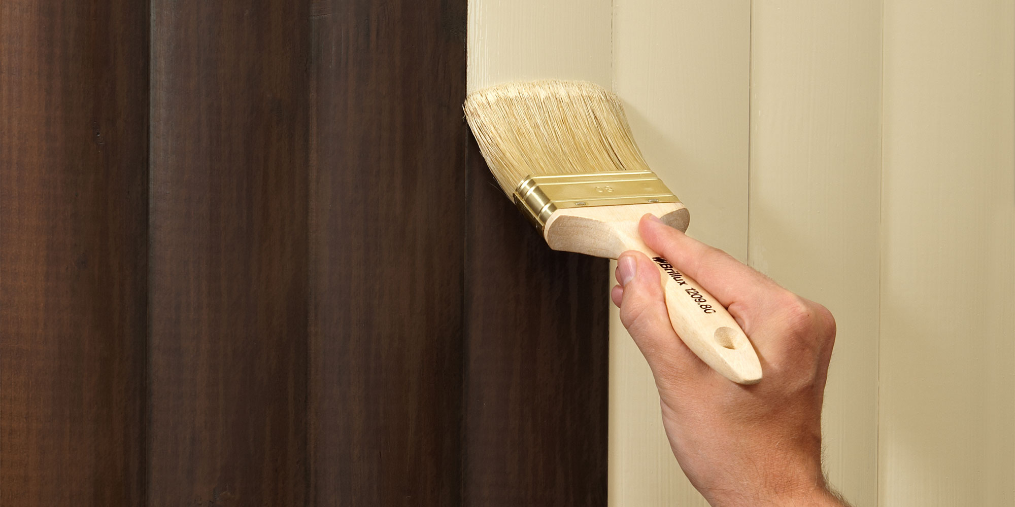 Hand trägt mit Pinsel eine helle Farbe auf dunkle Holzoberfläche auf, um einen gleichmäßigen Farbton zu erzielen