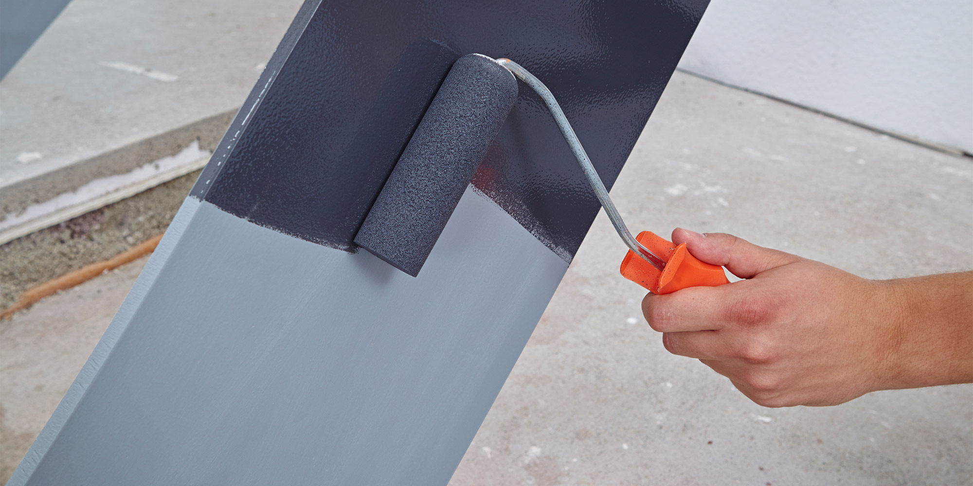 Rolle trägt grauen Lack auf Metallfläche auf, gleichmäßiger Anstrich auf schräger Platte