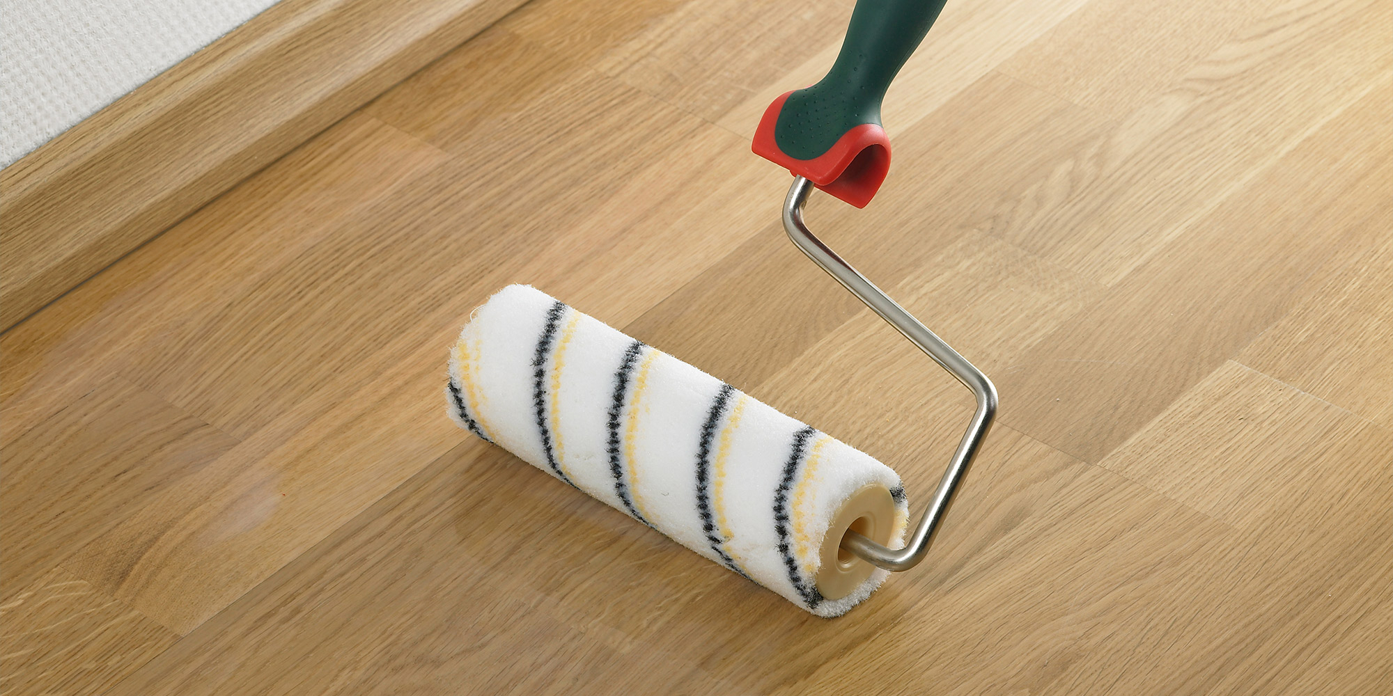 Farbrolle fuer Wandfarbe liegt auf einem Holzboden