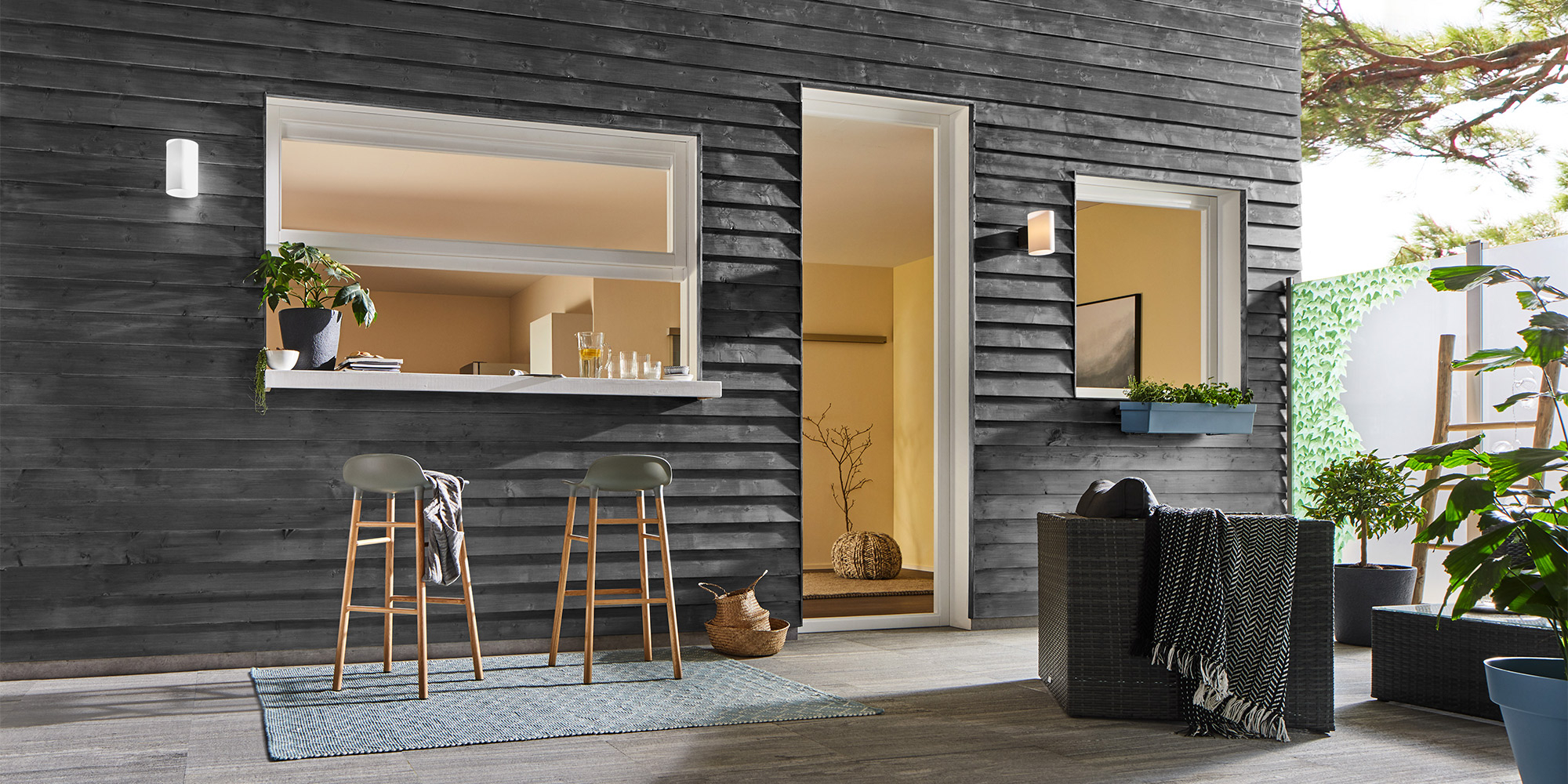 Terrasse vor schwarzer Holzfassade mit Durchreiche, Barhockern und Sitzmöbeln