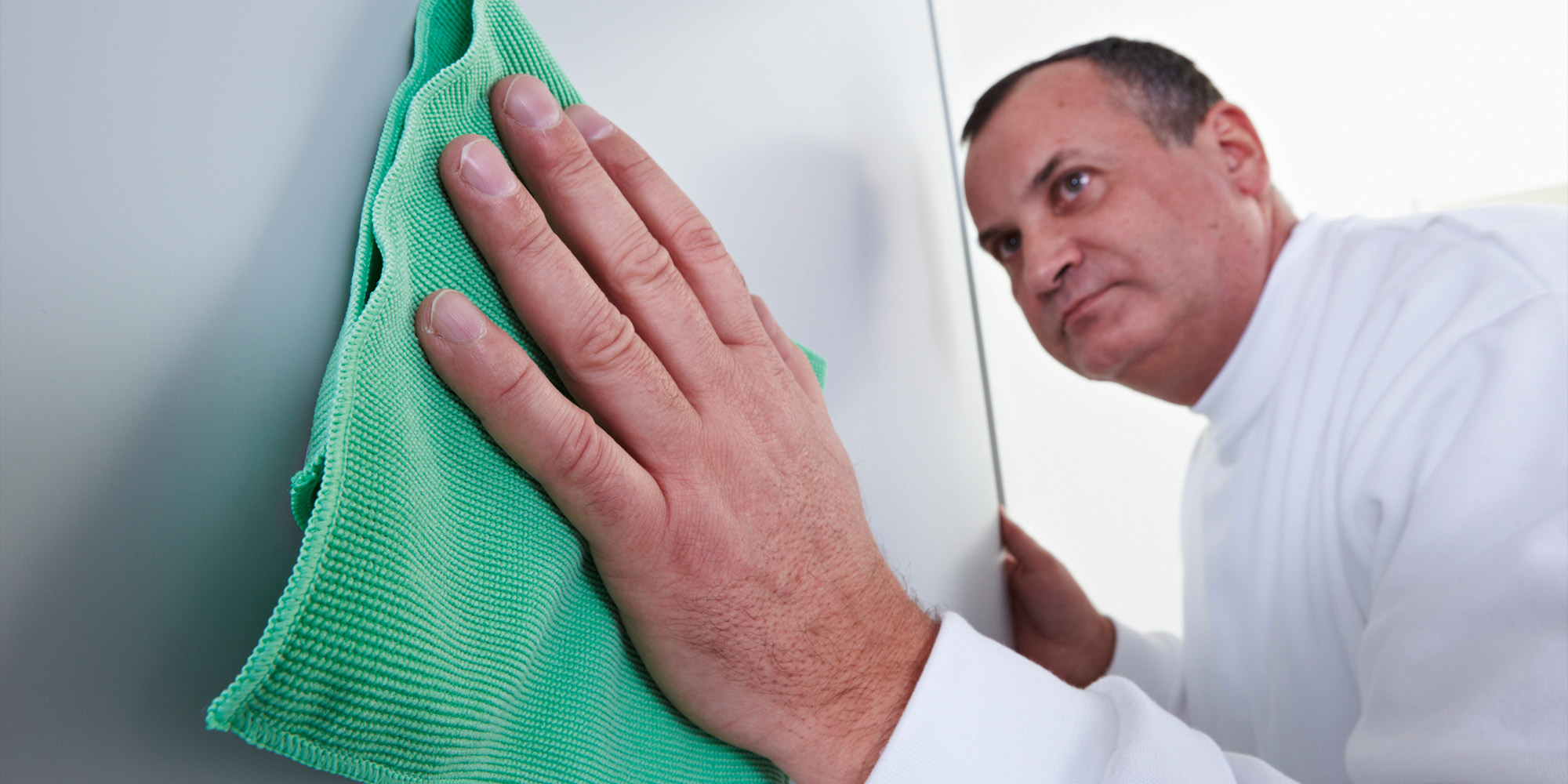 Hand reinigt eine glatte Oberfläche mit grünem Tuch, Vorbereitung für Klarlack Auftrag