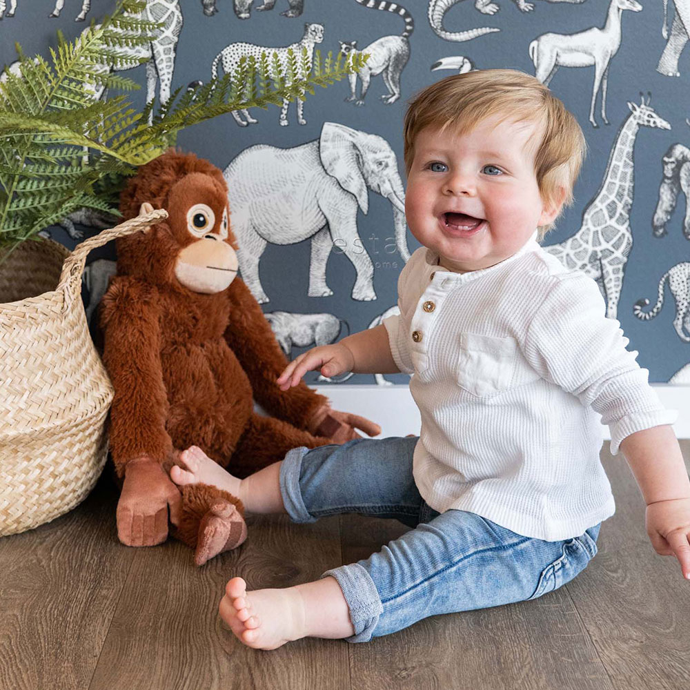 Ein kleiner Junge sitzt auf dem Boden vor einem Affen Kuscheltier und einer blauen Tapete mit Tieren.