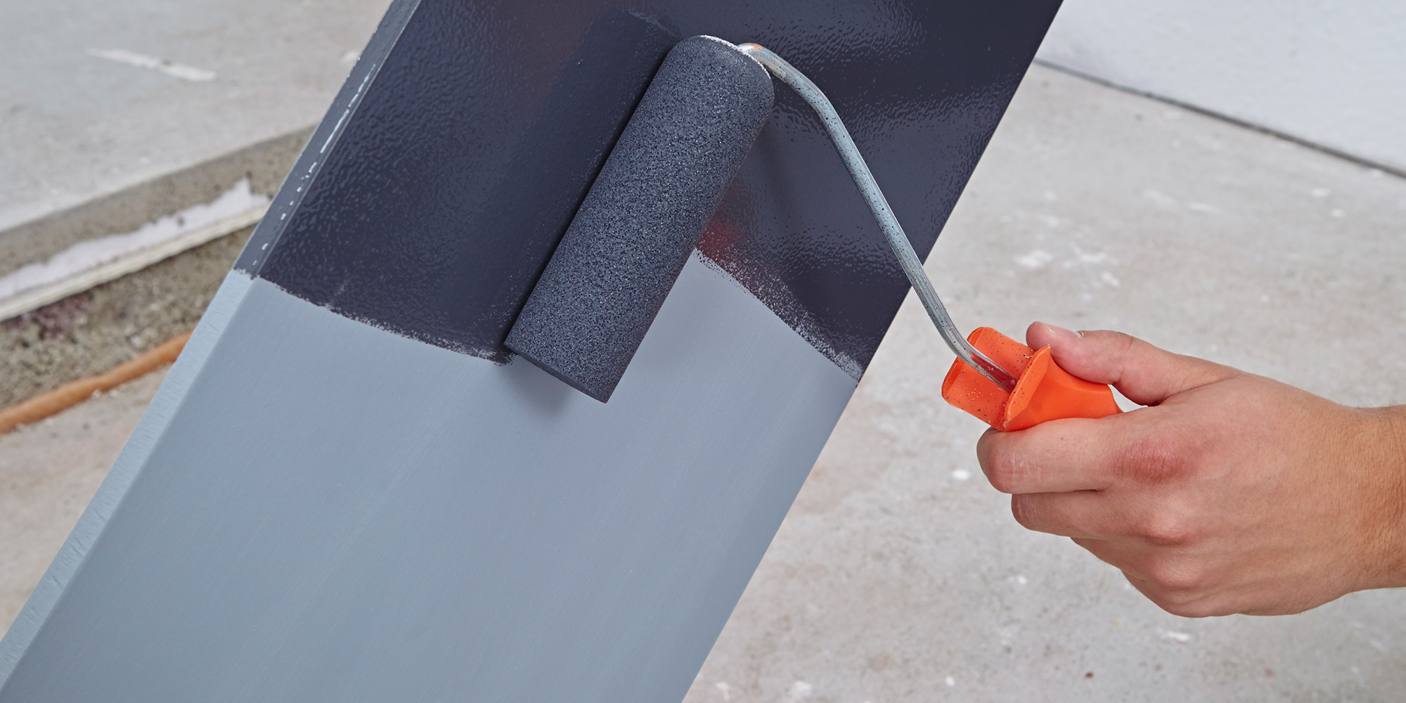 Hand mit Farbroller trägt anthrazitfarbene Sikkens Farbe auf eine Fläche auf