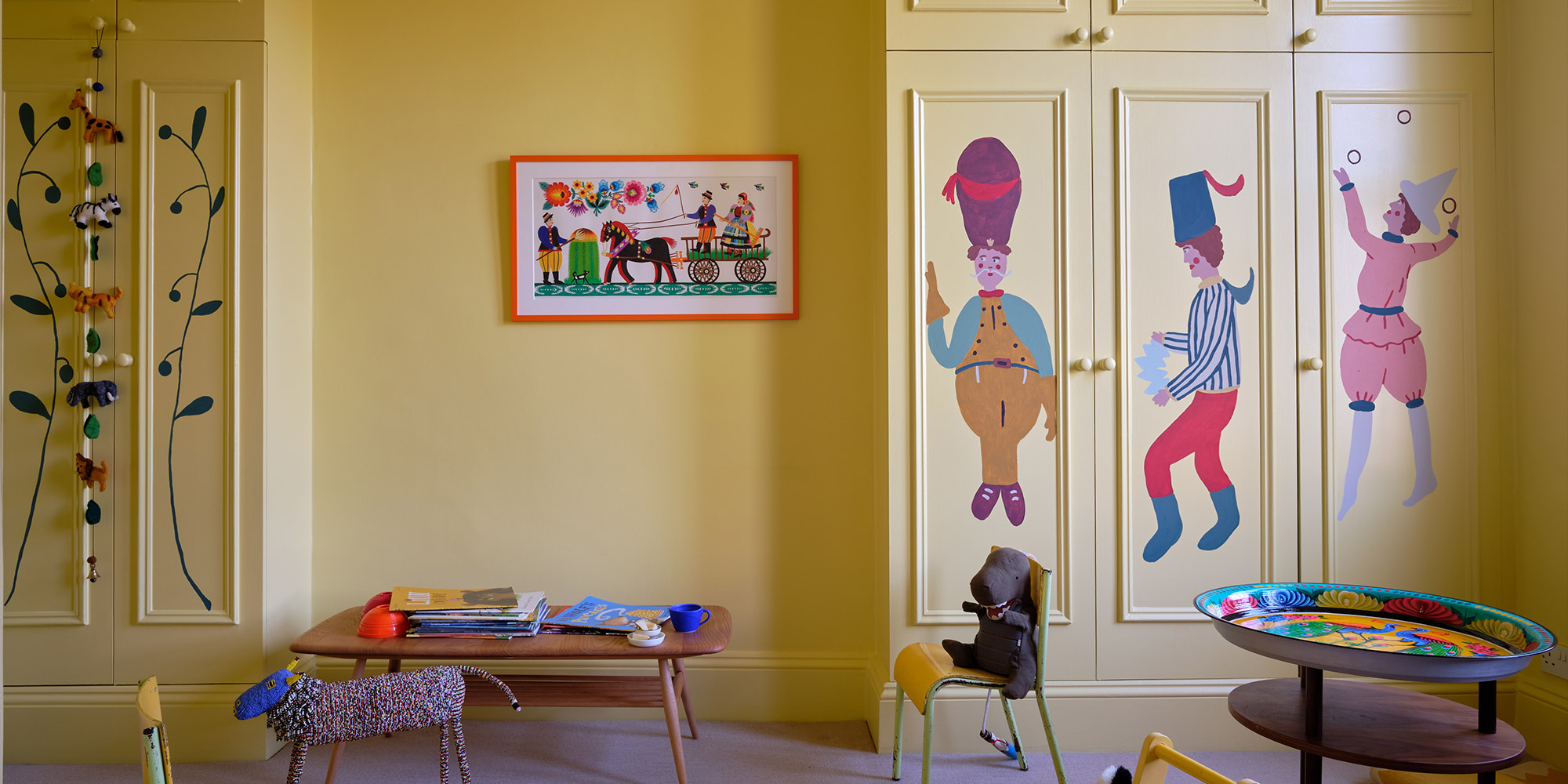 Kinderzimmer mit gelb gestrichenen Einbauschränken und bunten Figurenmotiven auf den Türen