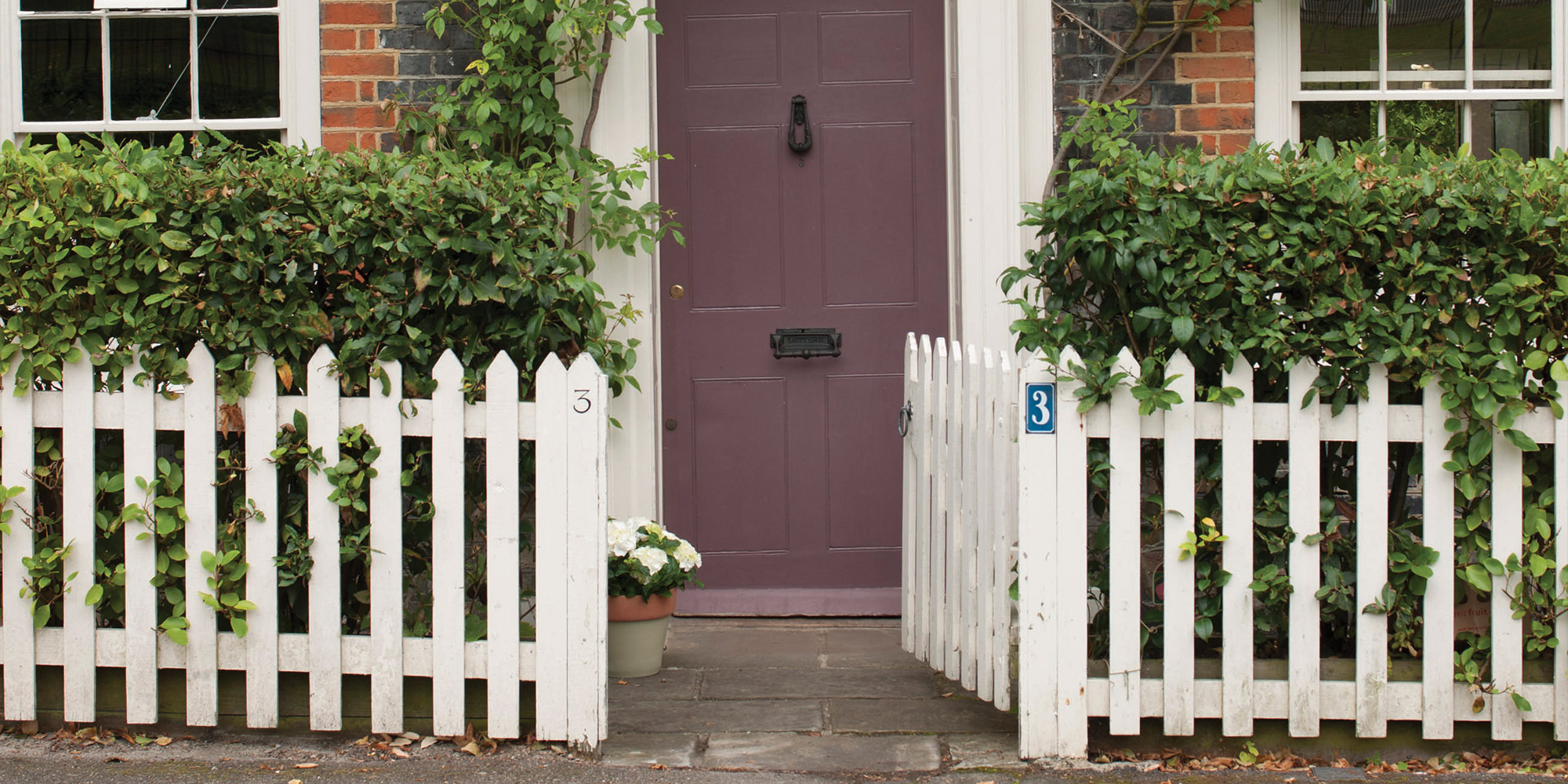 Weißer Gartenzaun mit offenem Tor vor Hauseingang und violetter Tür
