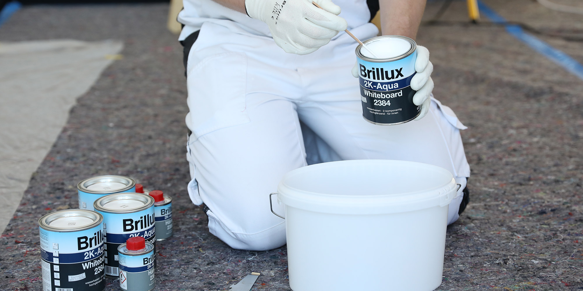 Maler mischt Brillux 2K Aqua Whiteboard 2384. Lackdose und Mischbehaelter auf dem Boden