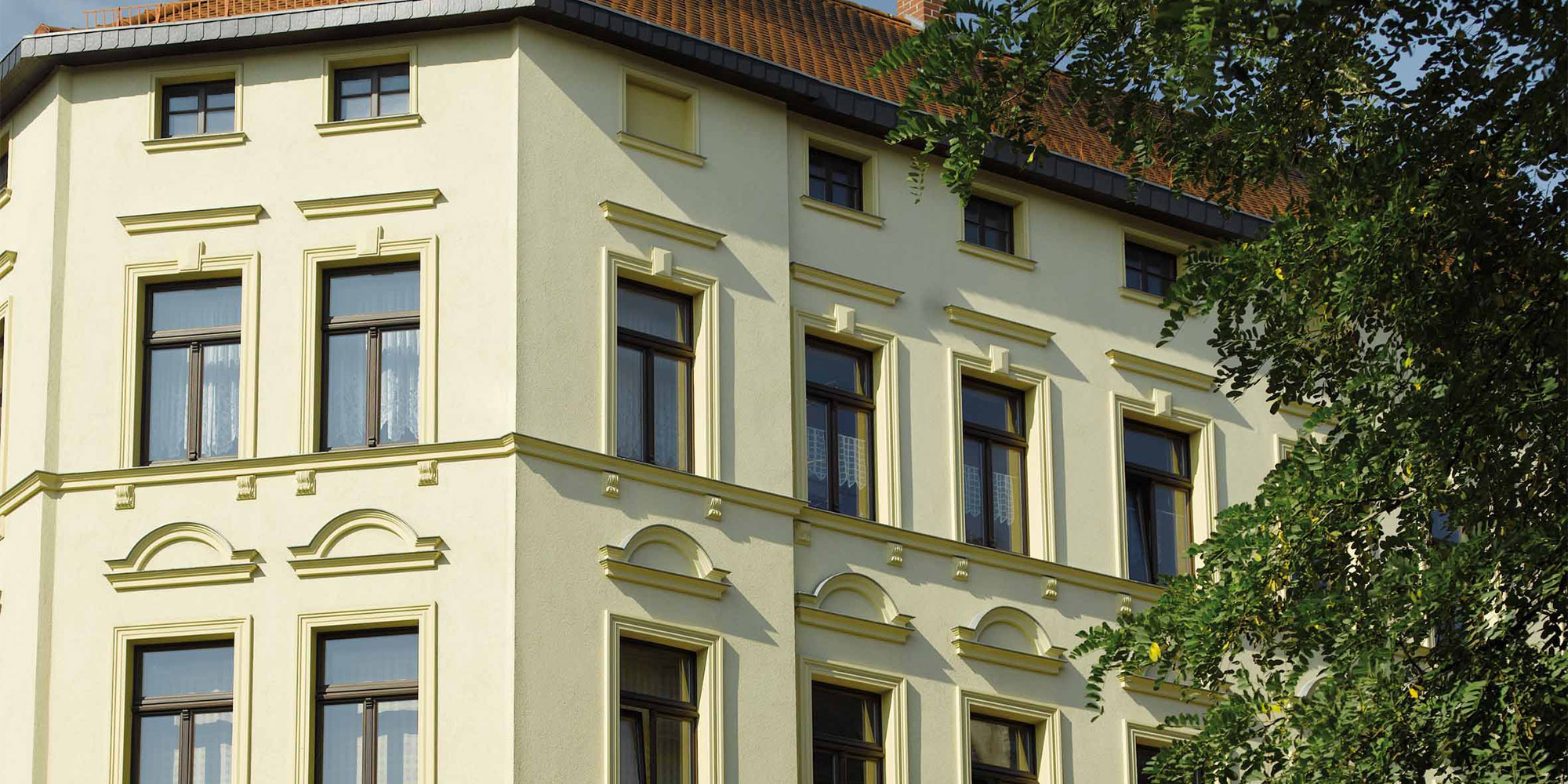 Altbau mit gelber Fassade und aufwendig verzierten Fensterprofilen aus Stuck Historische Fassadengestaltung mit aufwendig profiliertem Außenstuck