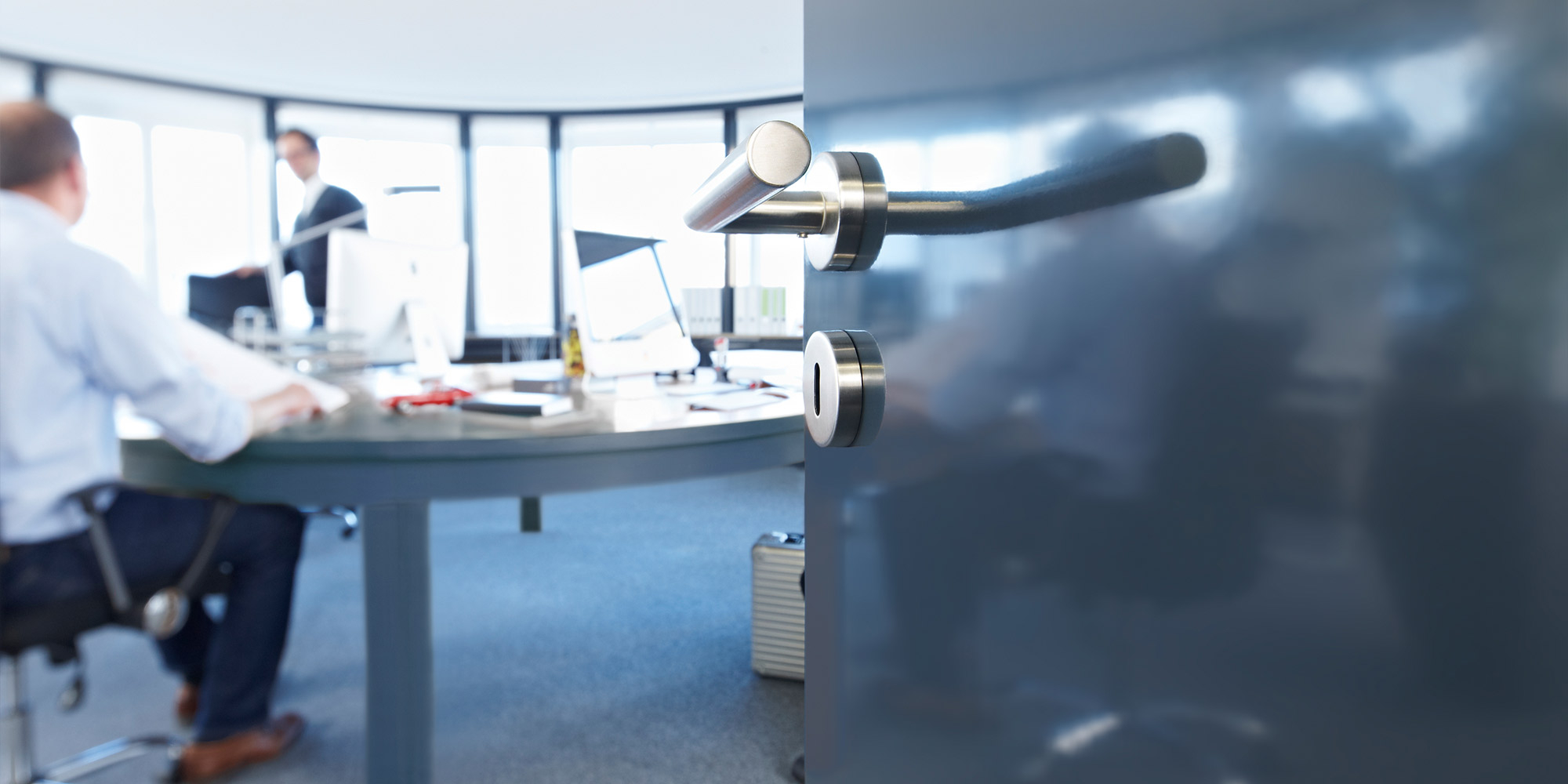 Geöffnete Tür mit glänzendem Lack in einem modernen Büro, im Hintergrund Menschen am Schreibtisch