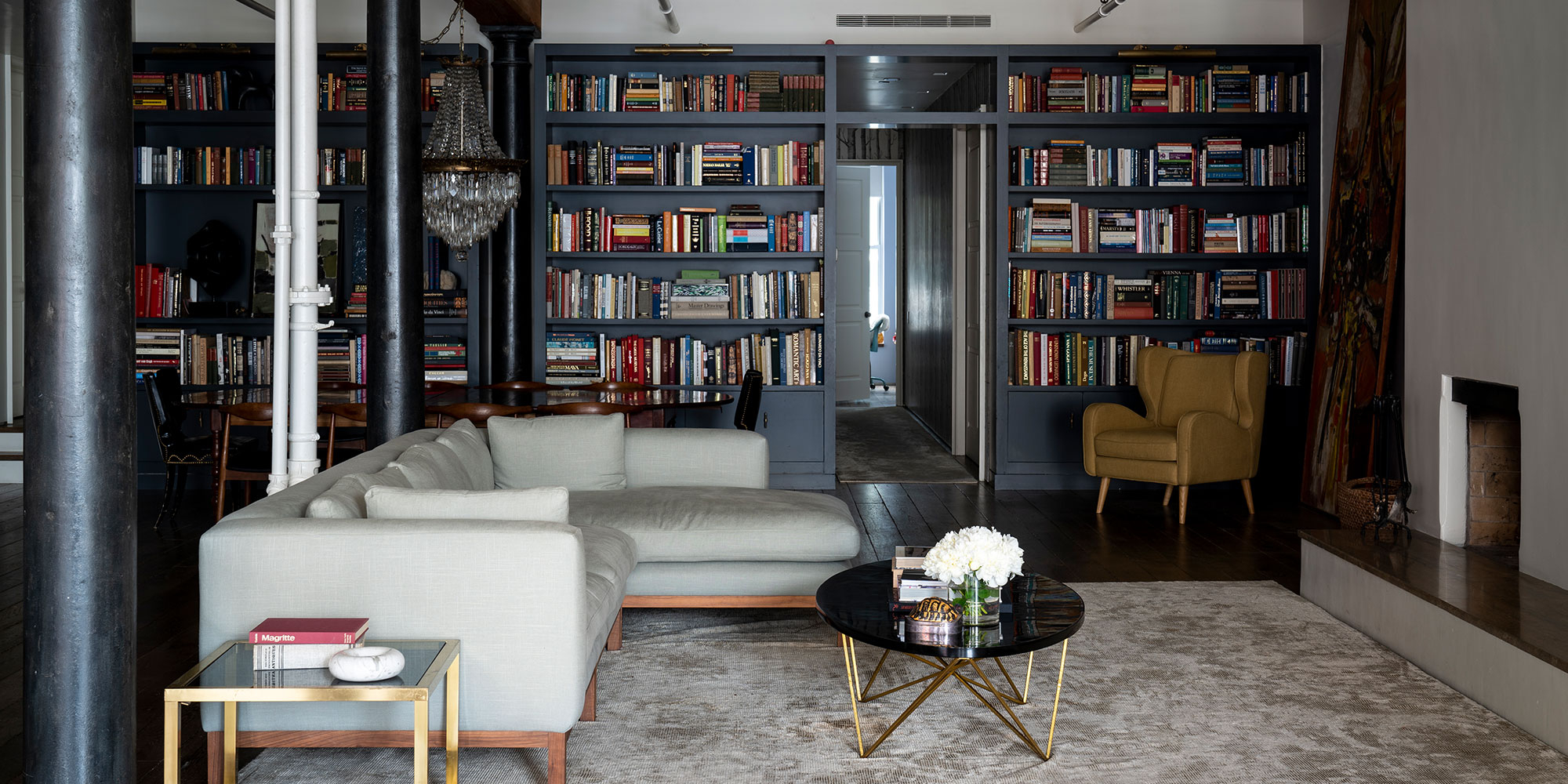 Wohnzimmer mit dunkelblauen Bücherregalen, hellem Ecksofa, rundem Couchtisch und Sessel