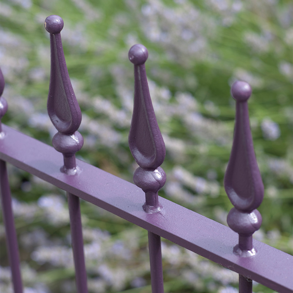 Nahaufnahme eines violett lackierten Metallzauns mit Zierspitzen vor Grün