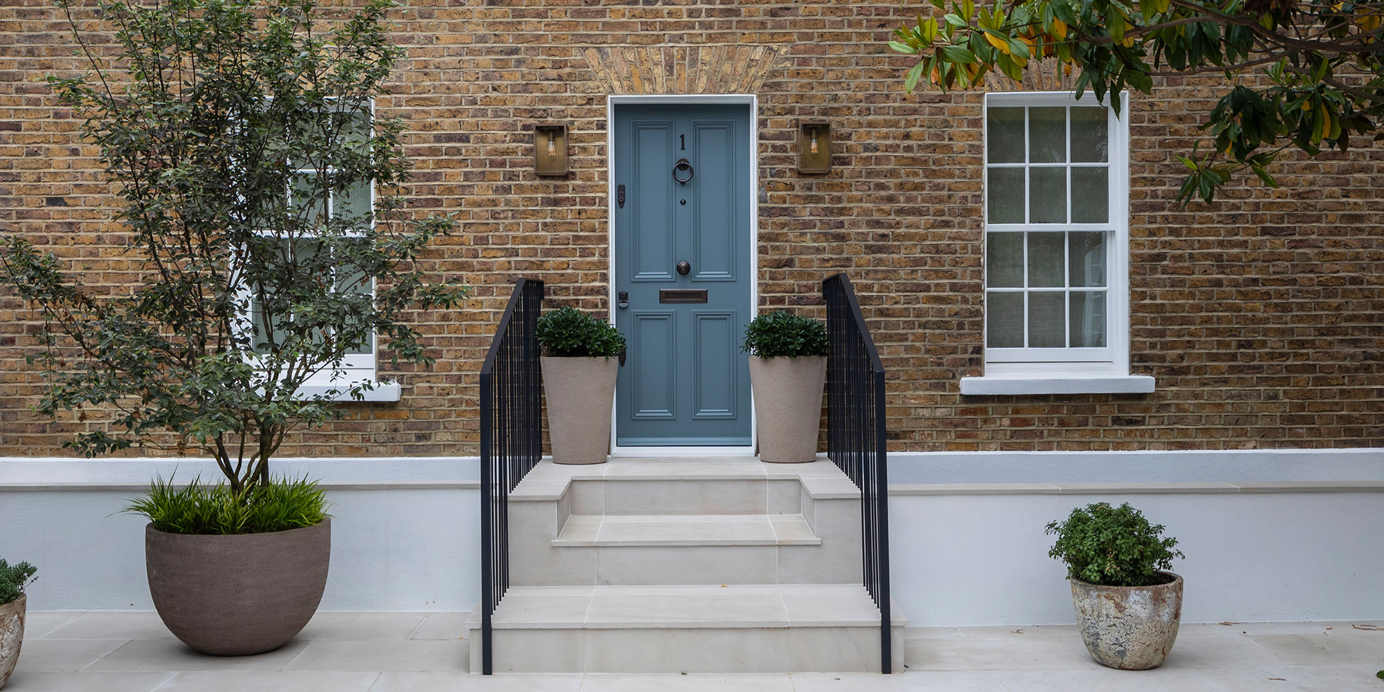 Mobile Headergrafik mit blaugrauer Haustür, Treppe und Pflanzkübeln vor Backsteinfassade - Haustüren streichen
