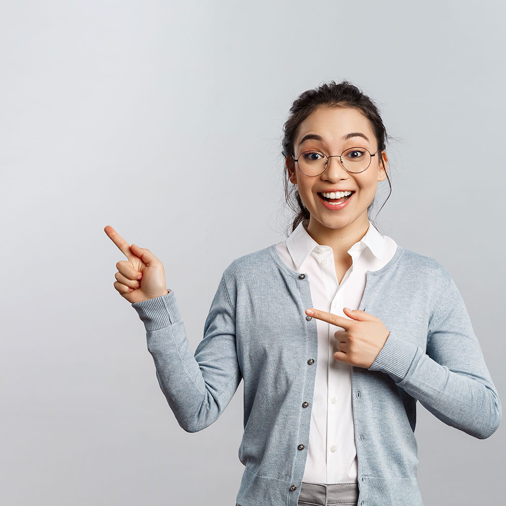 Junge Frau mit Brille zeigt lächelnd mit beiden Händen nach links auf einen freien Bereich, geeignet für Hinweise oder Tipps