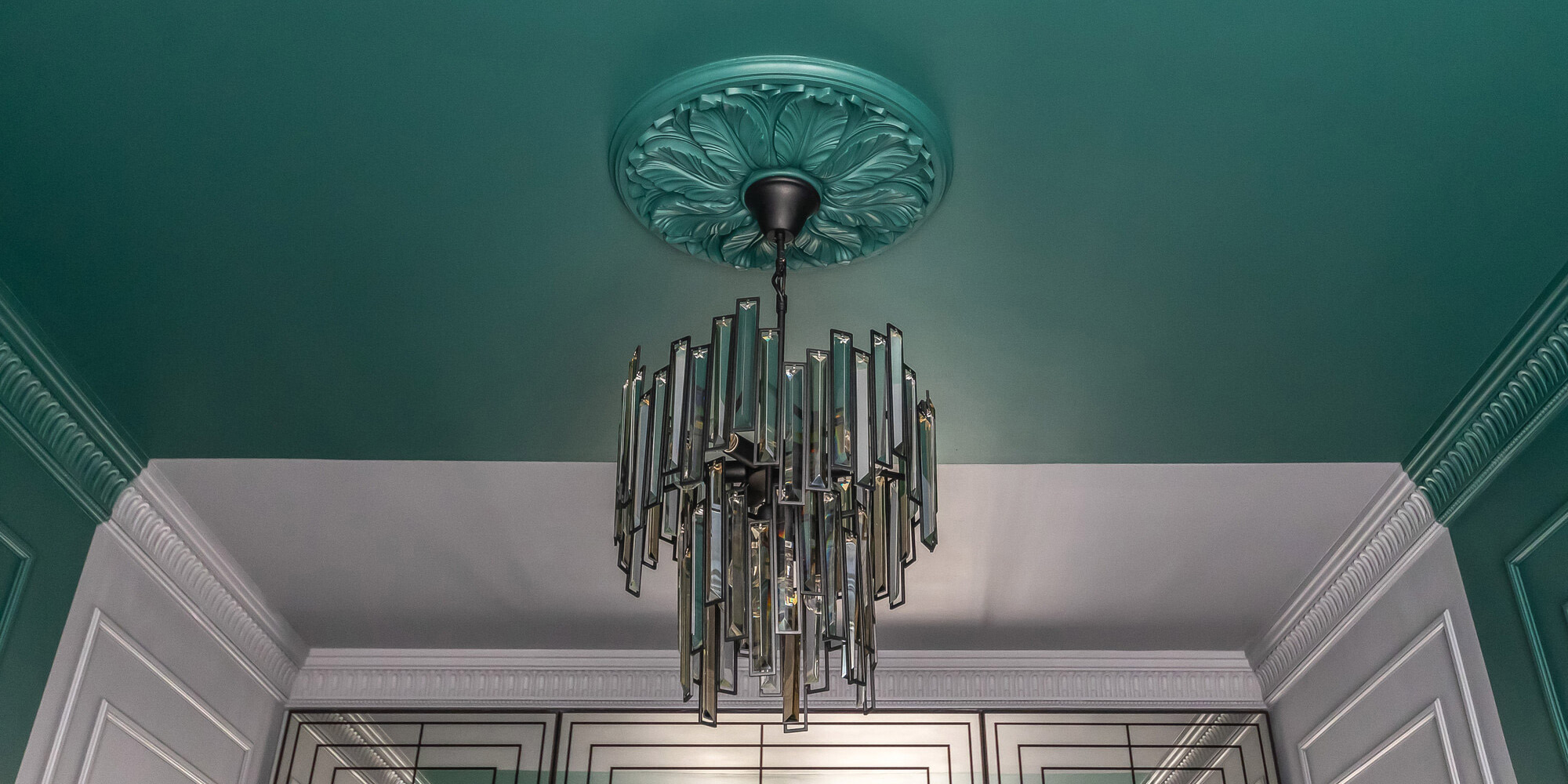 Eine große Deckenrosette im barocken Stil setzt einen exklusiven Kronleuchter im Wohnzimmer in Szene.