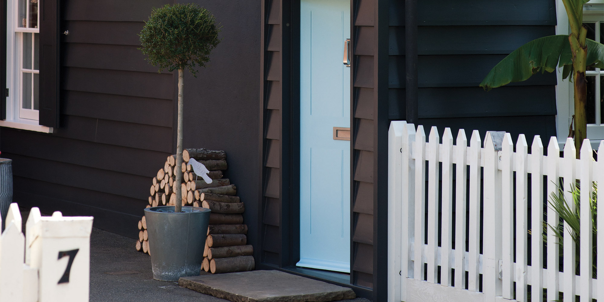 Schwarz gestrichene Holzfassade mit hellblauer Tür, weißem Zaun und gestapeltem Holz